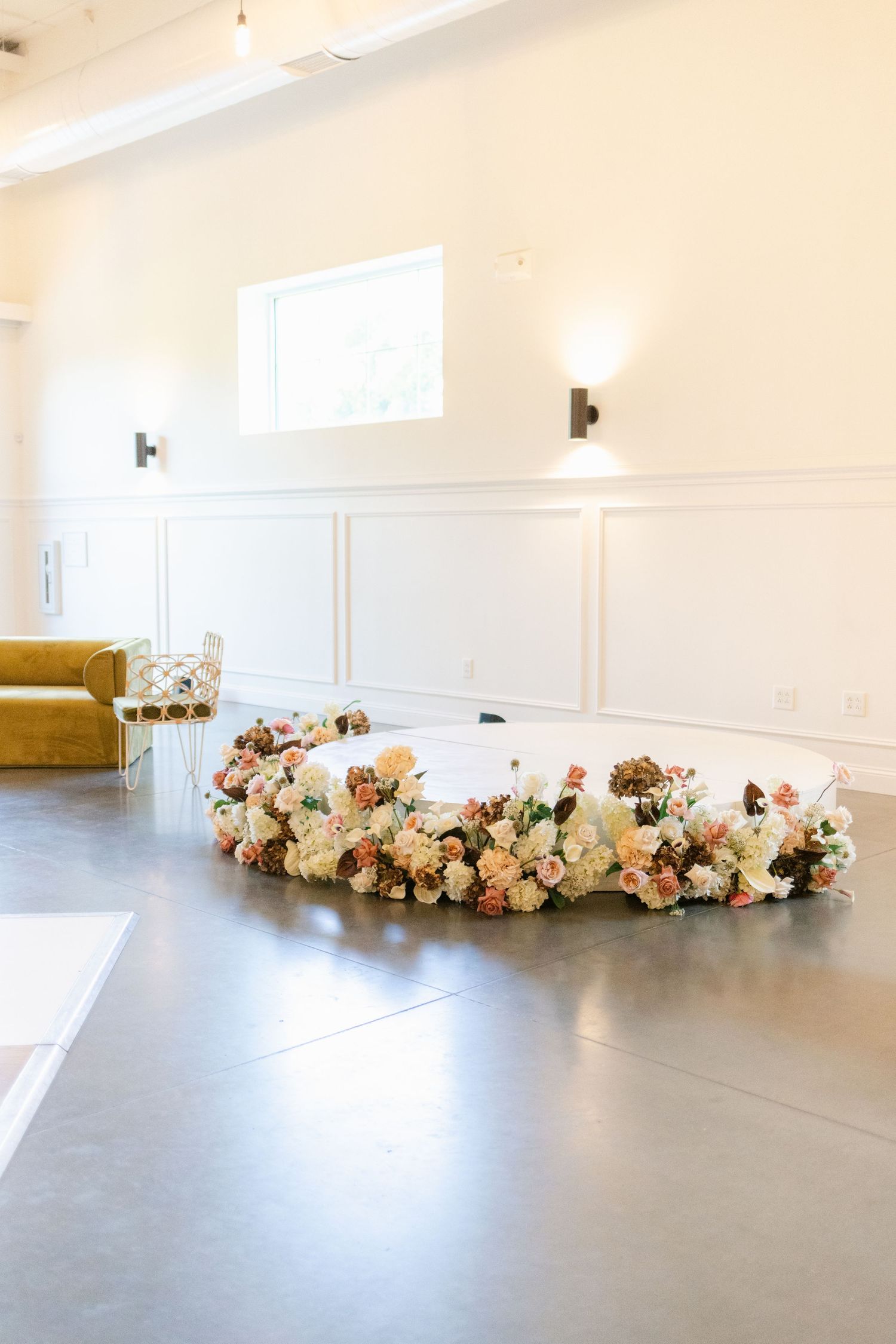 A curved floral arrangement with pink and white roses lines the floor against a white wall in a dance studio.