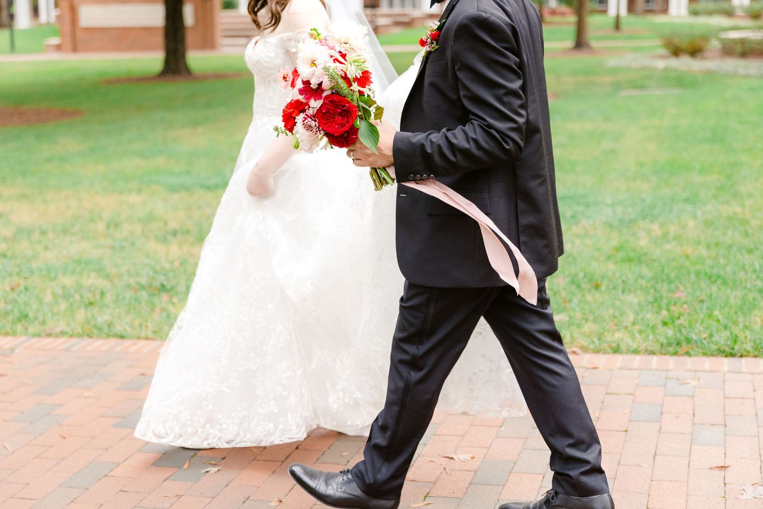 A couple walking together on a brick pathway in a garden setting during a wedding celebration.