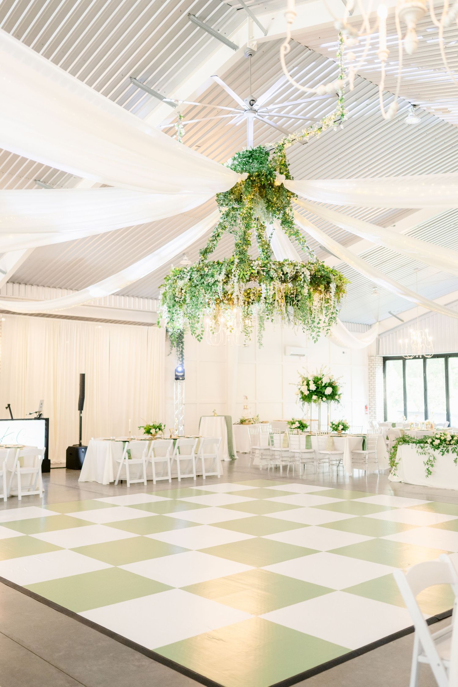 Modern white reception venue with checkered dance floor and hanging greenery decorations.