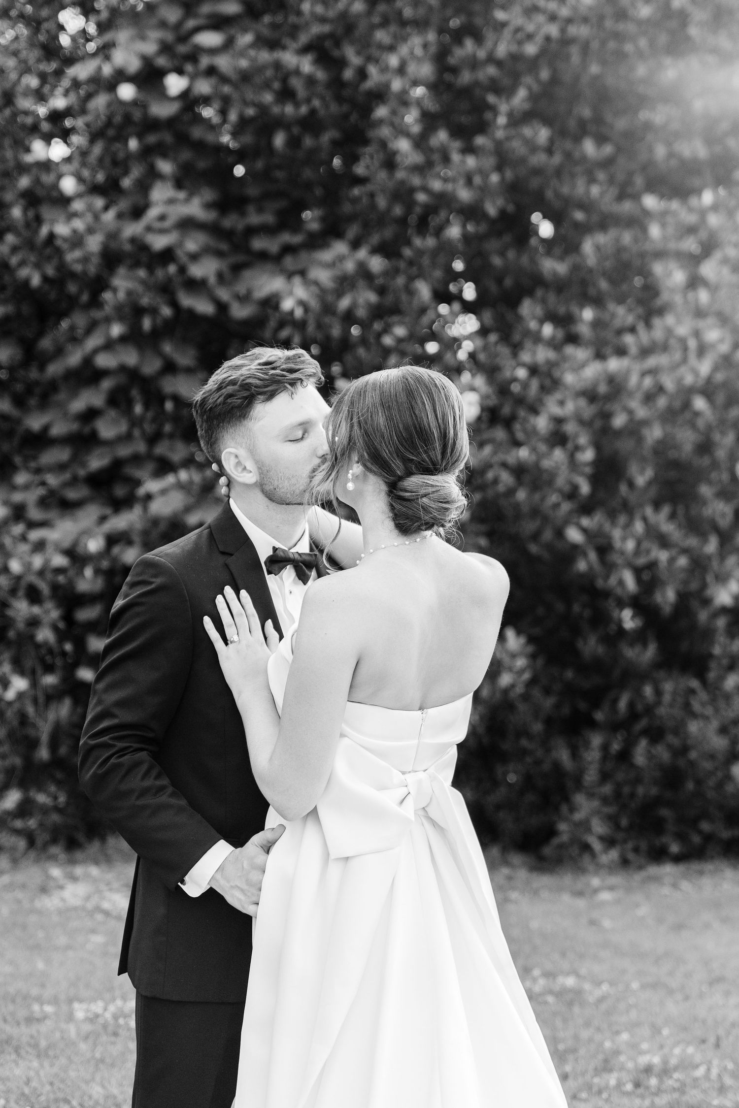 Black and white wedding portrait showing a romantic moment in front of garden foliage.