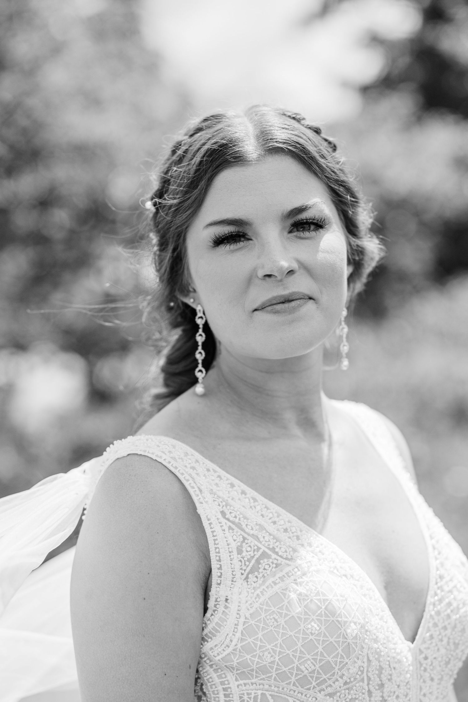 Elegant bridal portrait showcasing intricate lace dress, sparkling earrings and soft makeup.