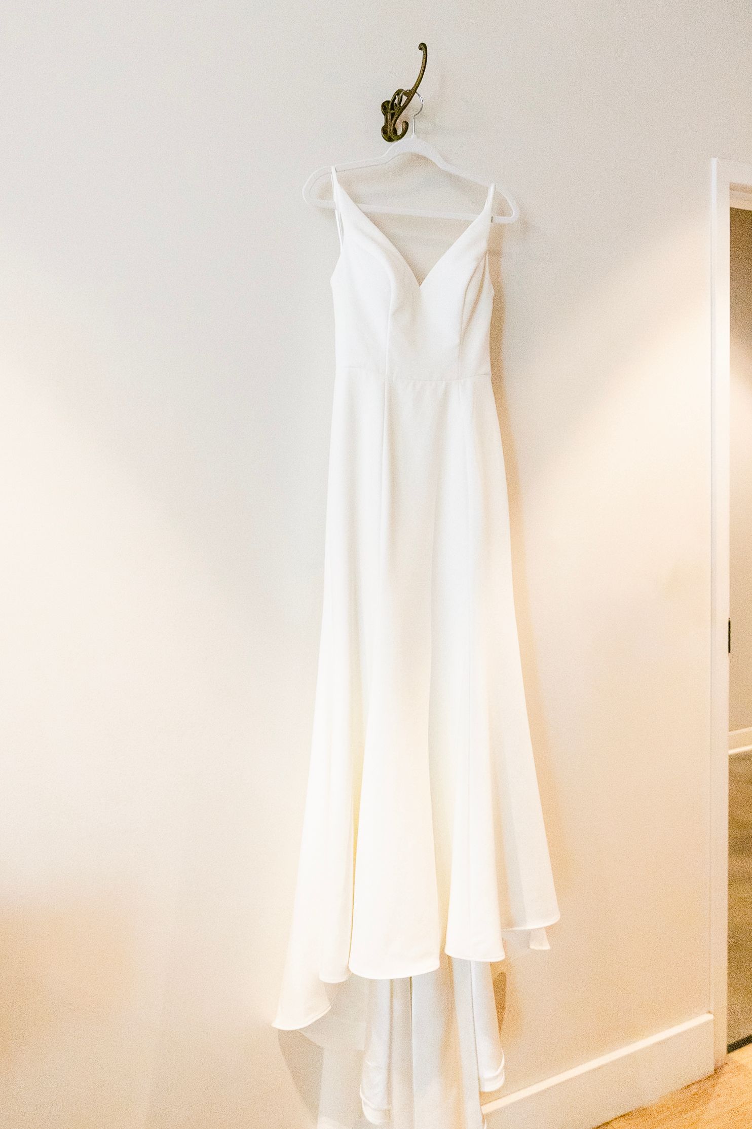 An elegant white wedding dress with spaghetti straps hangs on display against a neutral wall.