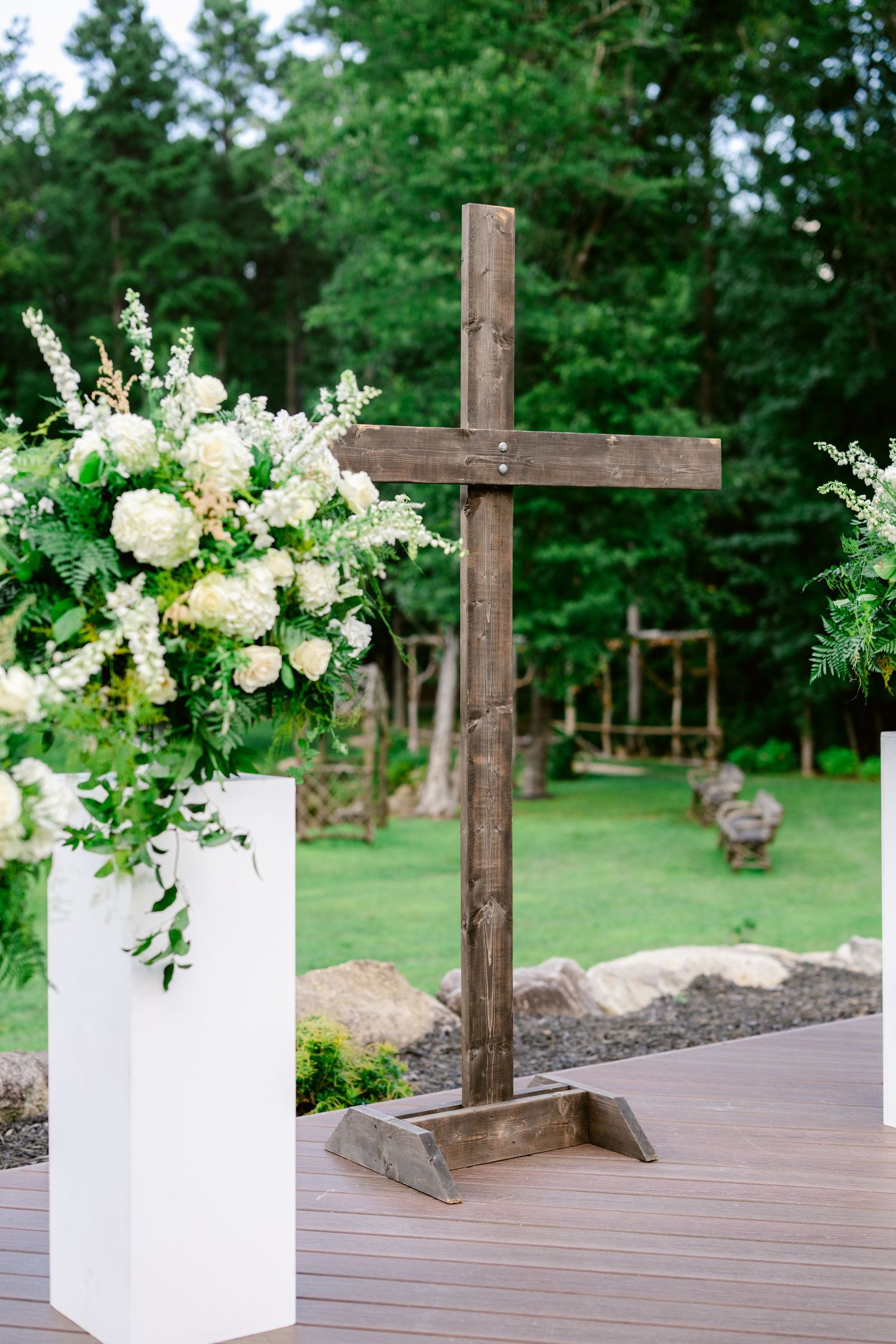 A series of decorative wooden crosses and white floral arrangements displayed on a wooden deck in an outdoor garden setting.
