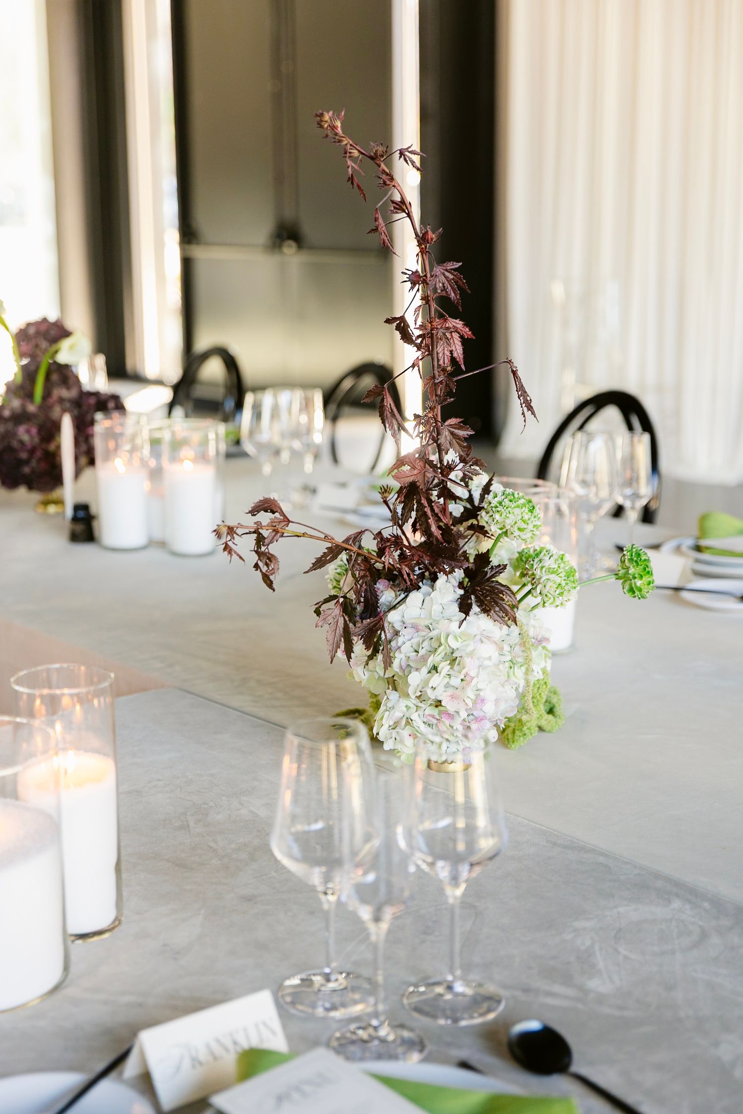 Long dining table with white tablecloth decorated with delicate floral arrangements and glowing candles.