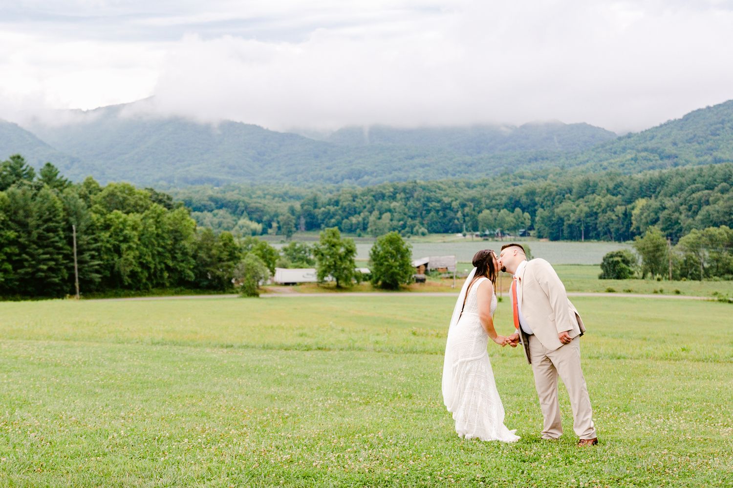 A couple shares a romantic moment on a hilltop overlooking mountains and valleys on their wedding day.