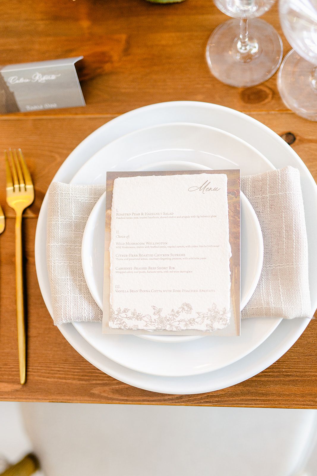 Close-up of formal place settings with white plates and printed menu cards on a wooden table surface.