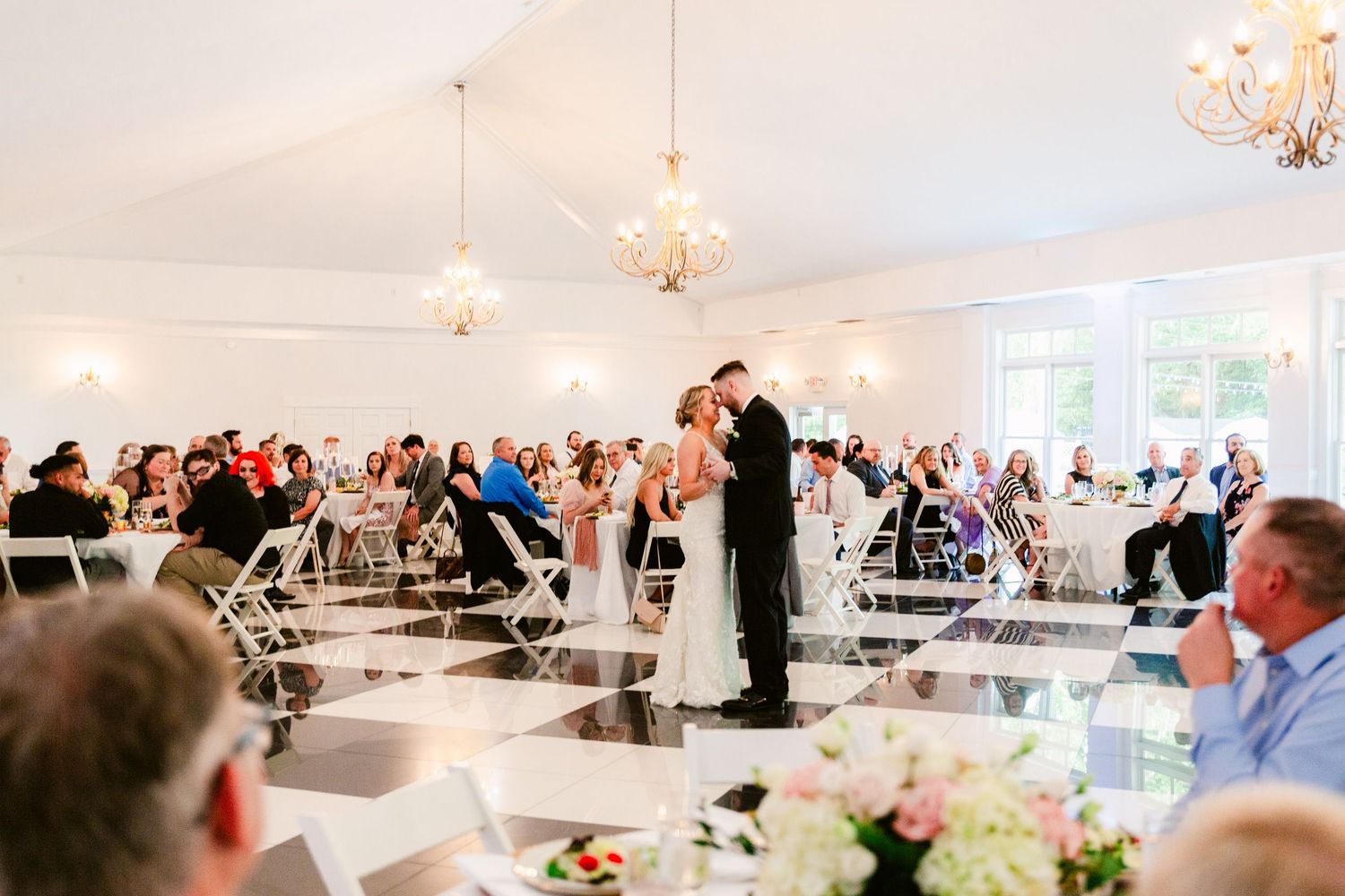 Wedding reception guests dine and socialize under an elegant white tent decorated with twinkling lights and floral arrangements.