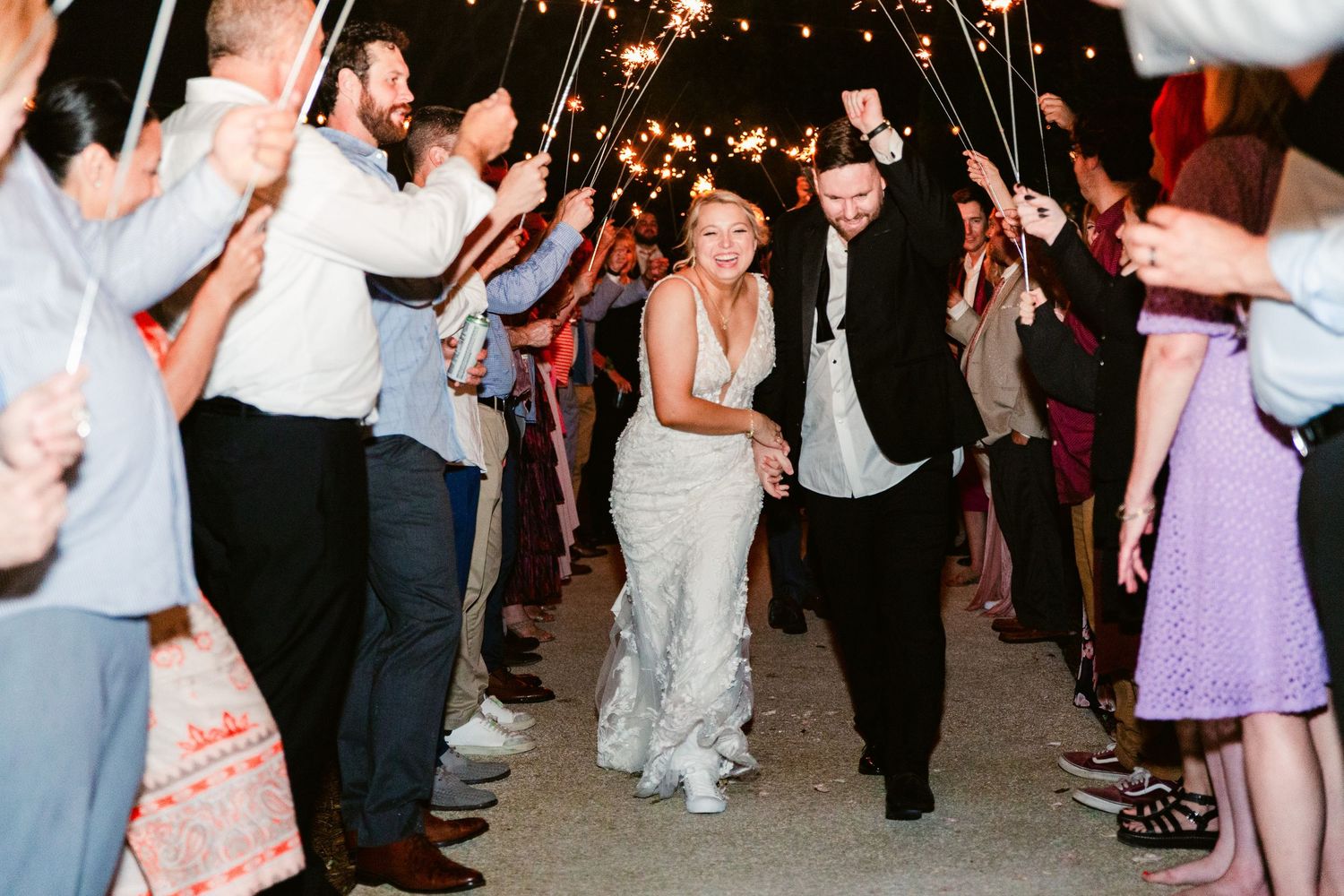 People dancing and celebrating at a wedding reception with string lights glowing overhead in a festive atmosphere.