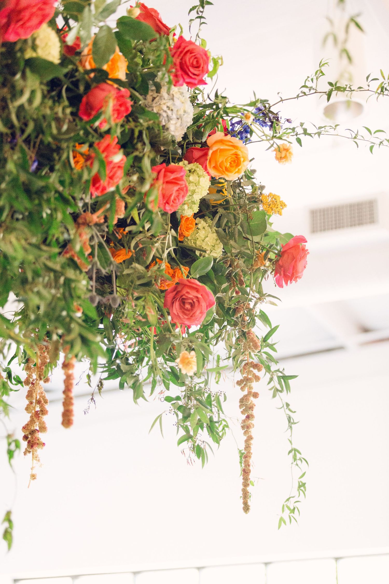 Lush floral arrangement with coral roses, orange blooms and cascading greenery hanging from above.