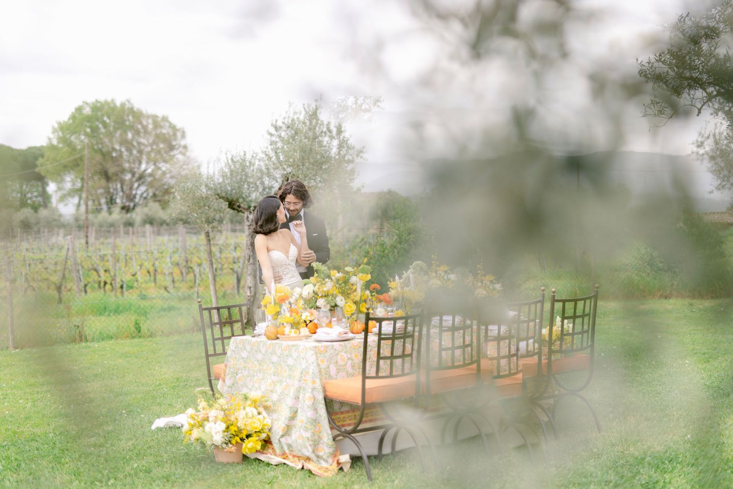 Elegant outdoor garden party setup with yellow floral arrangements and rustic chairs on a misty spring day.