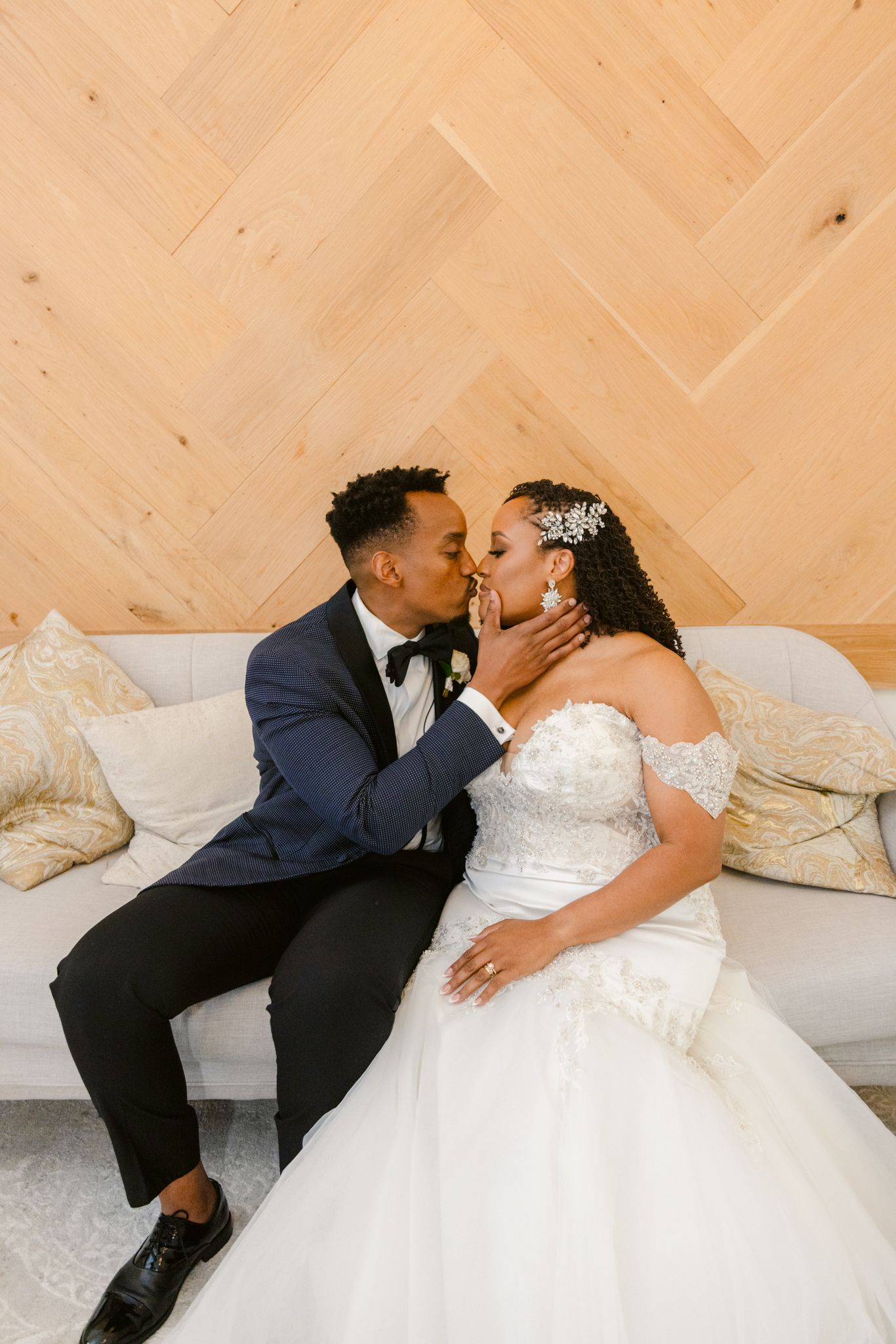 An intimate wedding moment shared on a couch with herringbone wood paneling in the background.