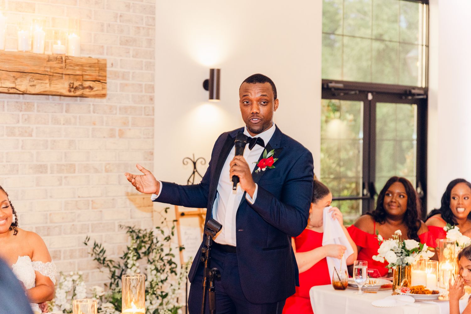 Wedding reception guests celebrate at an elegant venue with white decor and red floral accents.