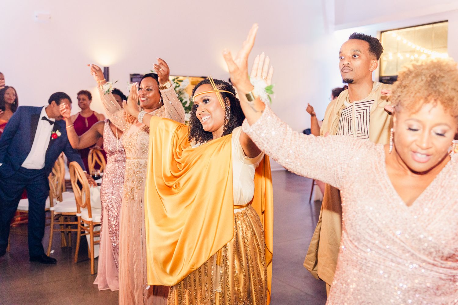 Wedding guests in formal attire dancing and celebrating with raised hands.