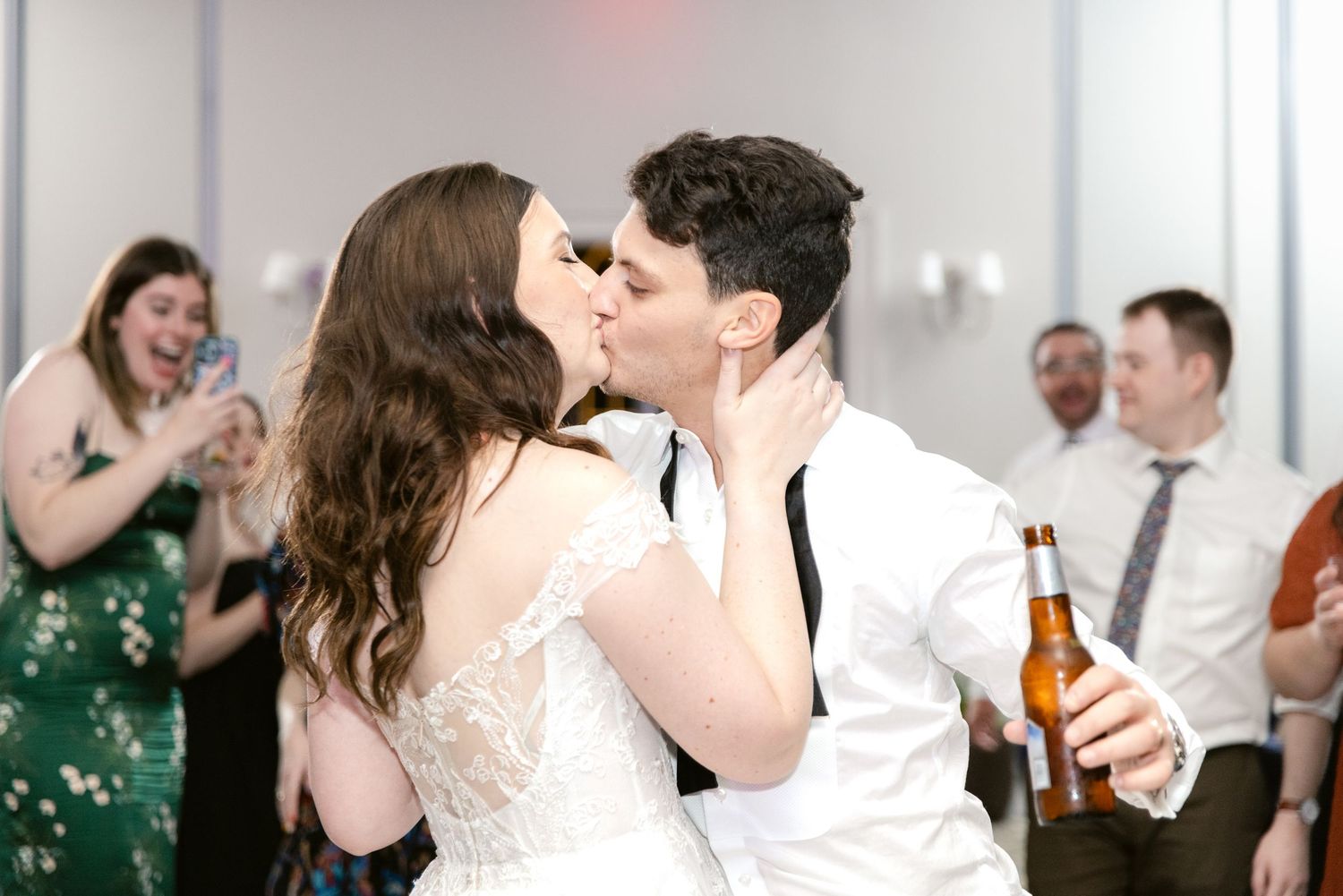 Wedding guests dance and celebrate while holding drinks on a lively reception dance floor.