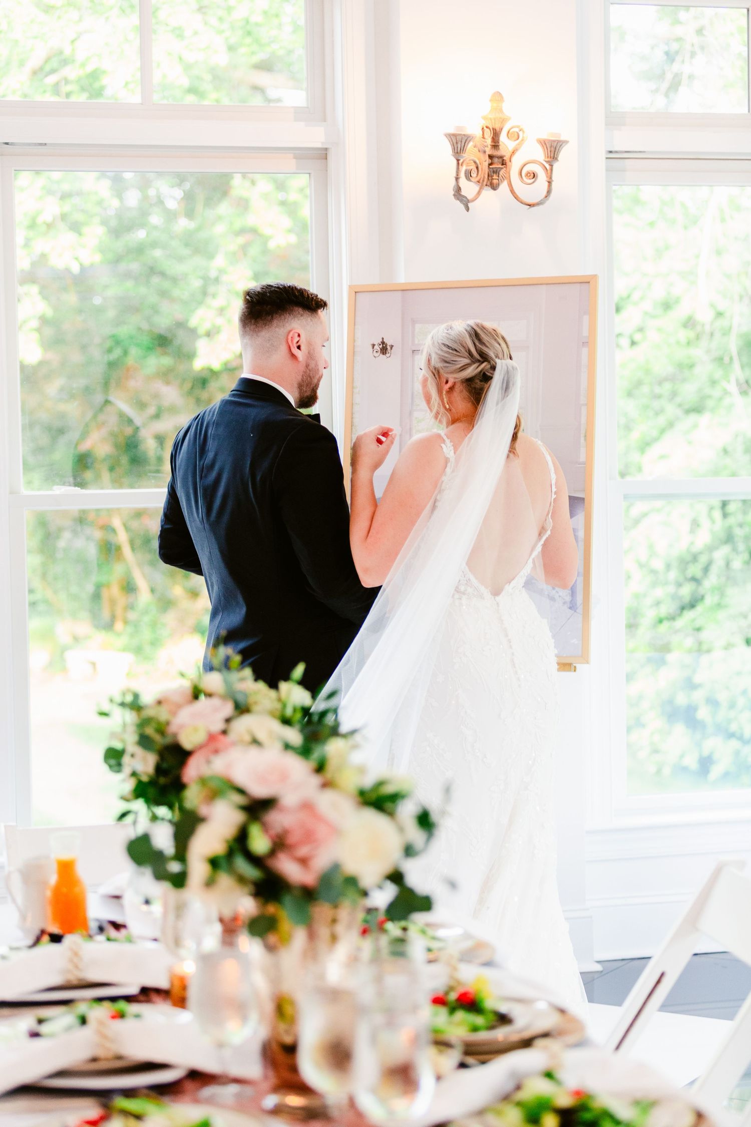 Elegant wedding reception setup with white linens, floral centerpieces, and natural light streaming through windows.