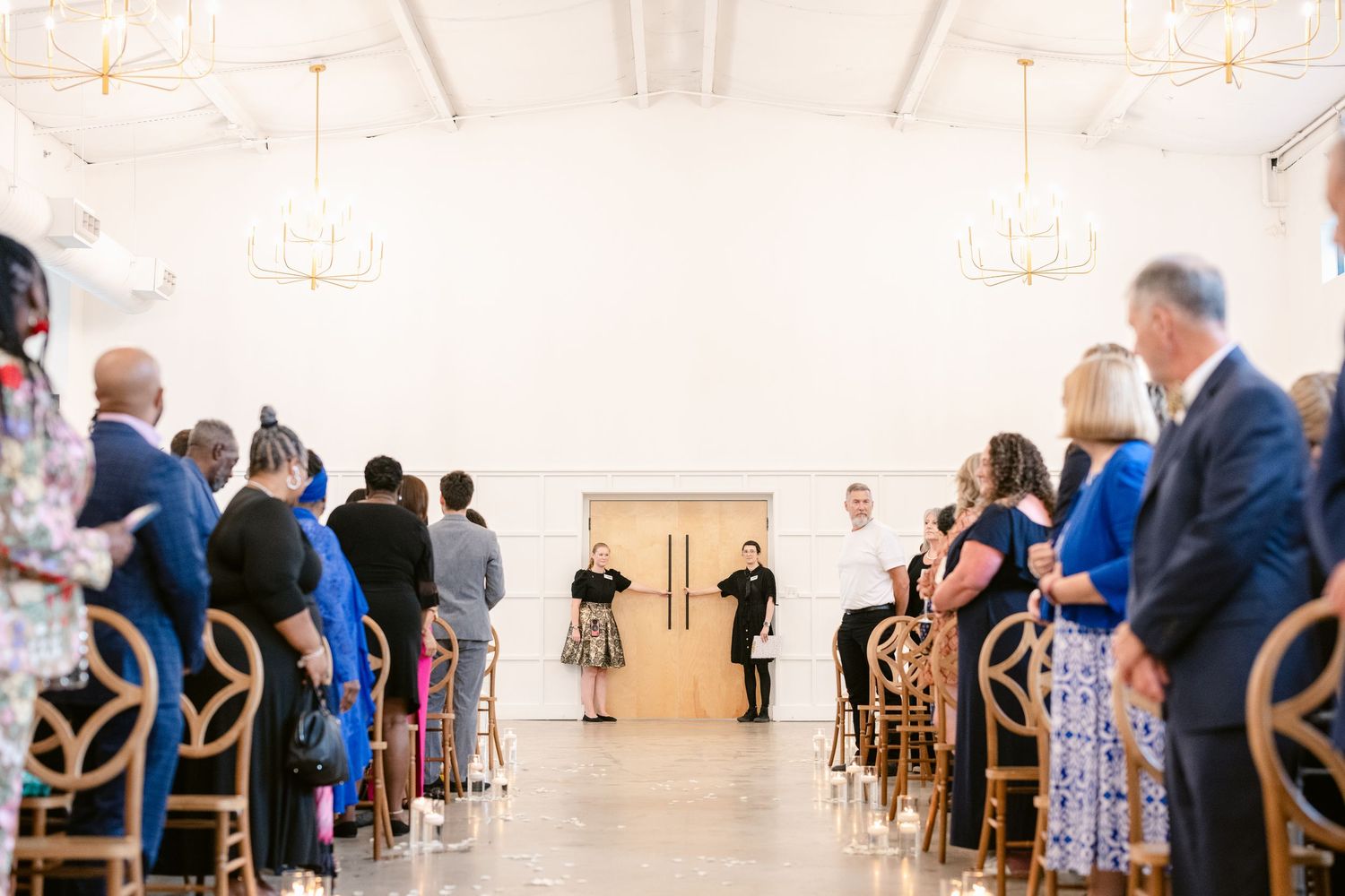 Wedding guests seated in rows of chairs in a bright white ceremony venue.