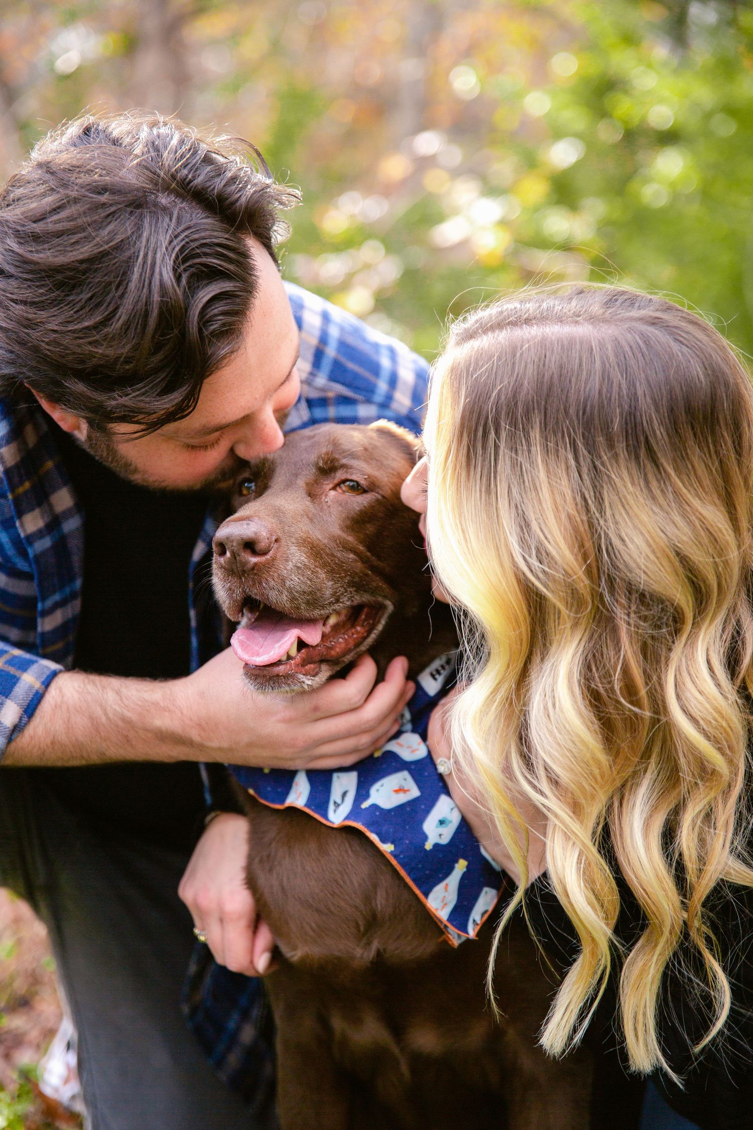A couple shares affectionate moments with their brown dog in an outdoor setting.