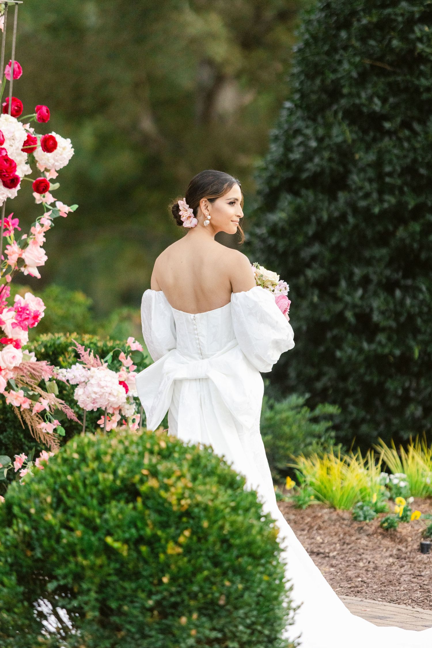 Elegant white dress contrasts with vibrant garden flowers and lush greenery in an outdoor portrait setting.