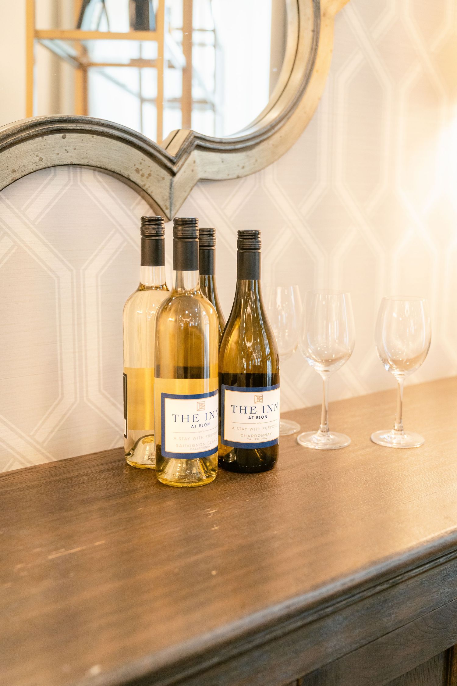 Wine bottles and glasses arranged on a wooden shelf with decorative wall panels in the background.