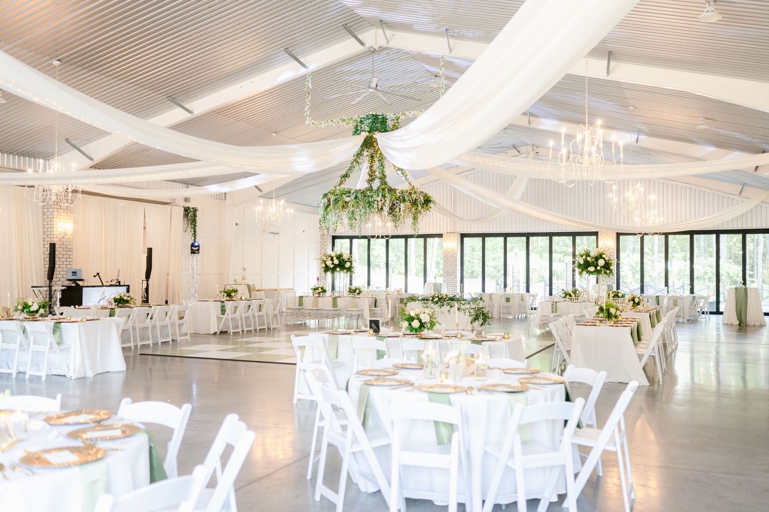 Spacious white reception hall with modern lighting fixtures and white chairs arranged around circular dining tables.