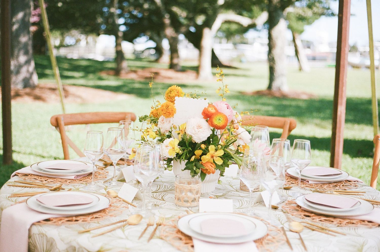 An elegant outdoor wedding table setting with floral centerpieces and cross-back chairs.