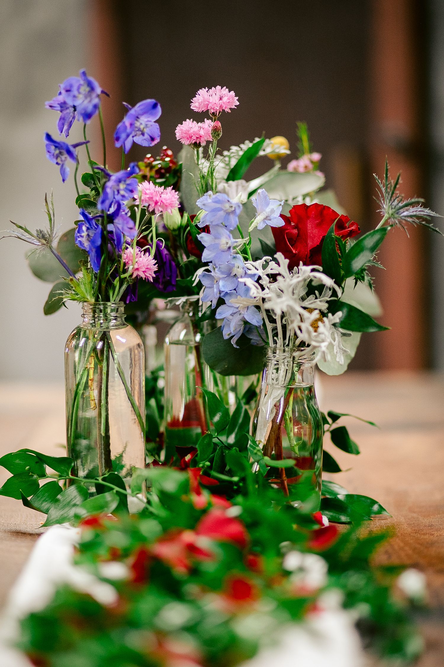 Colorful wildflower arrangements in glass bottles with greenery on wooden table.