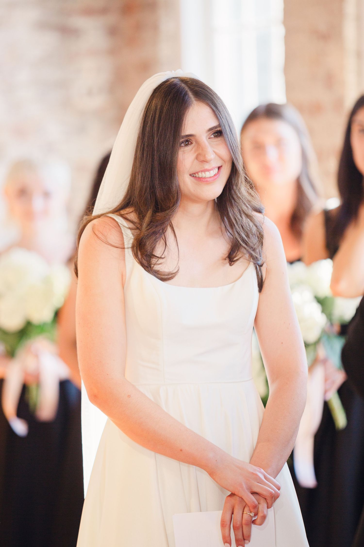 A person in a white wedding dress stands in an elegant venue with exposed brick walls.