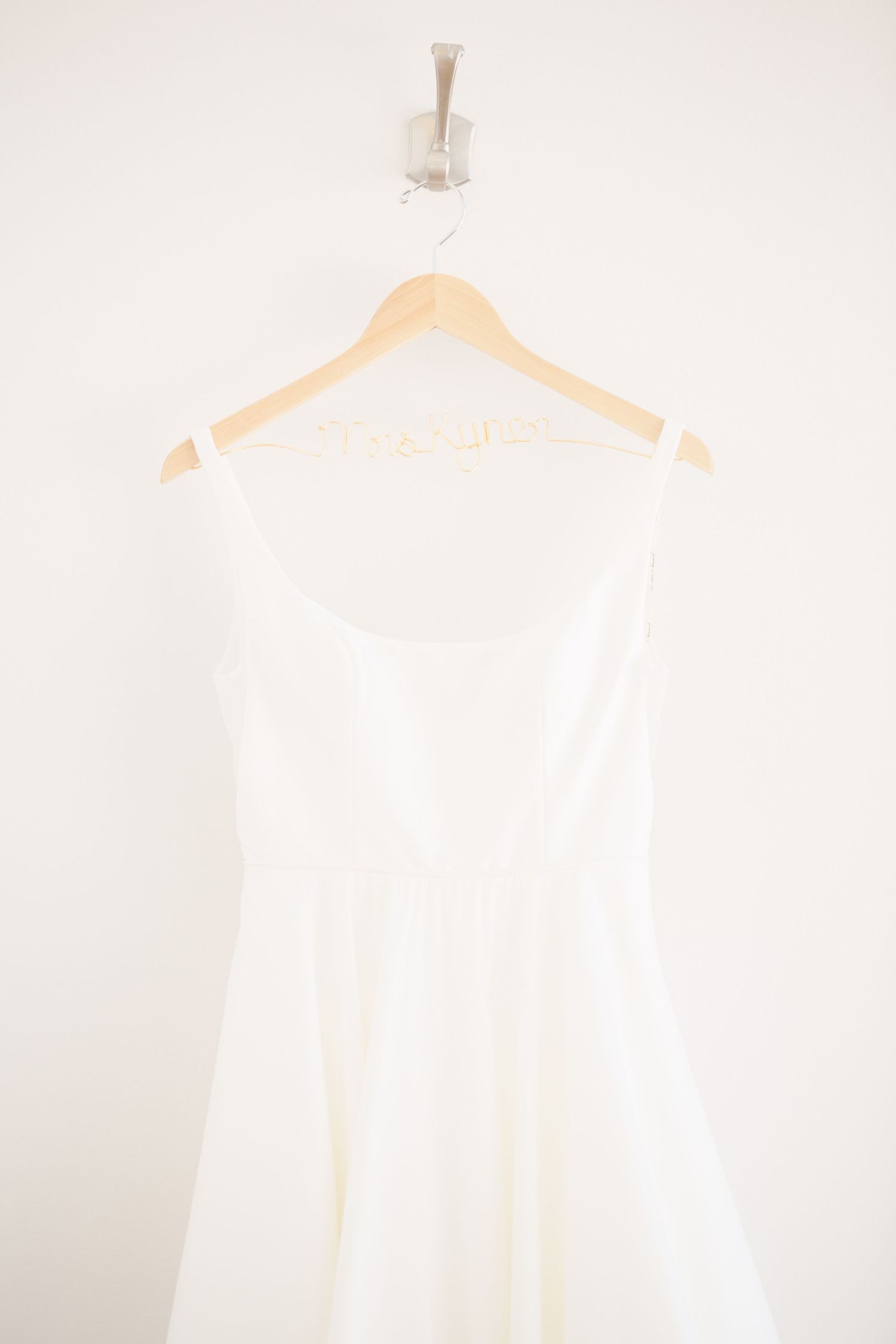 White wedding dress hanging on wooden hanger against light background.