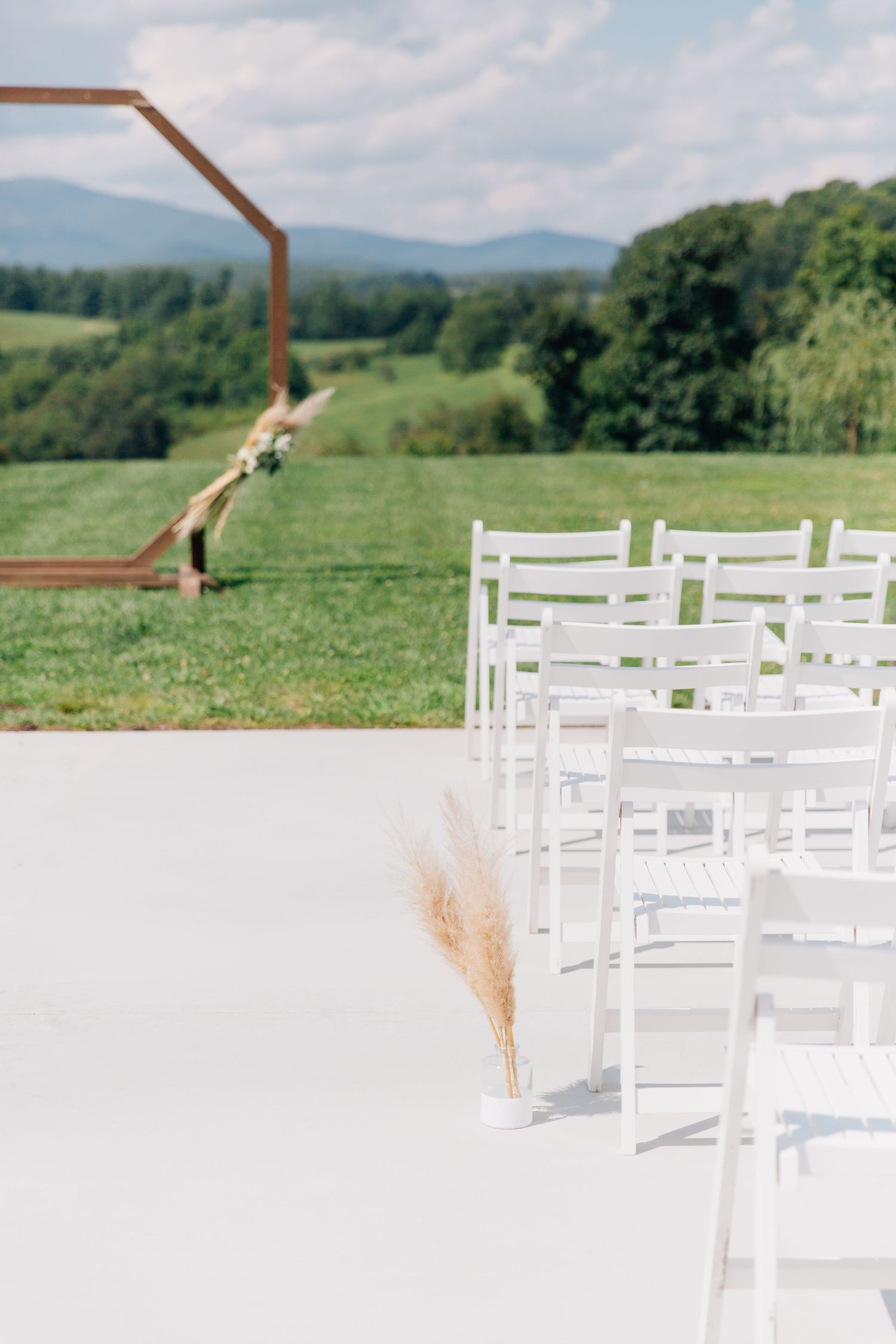 Modern wooden wedding arch and white chairs set against rolling mountain landscape.