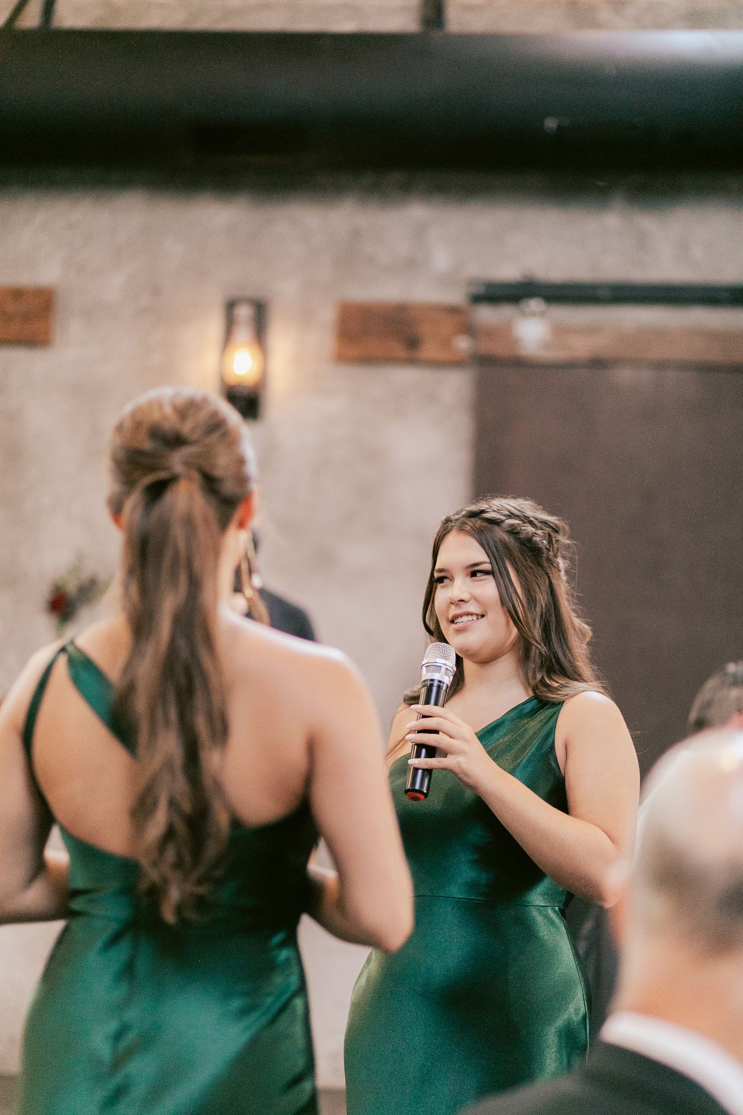 Bridesmaids in emerald green dresses give toasts at an elegant indoor reception venue.