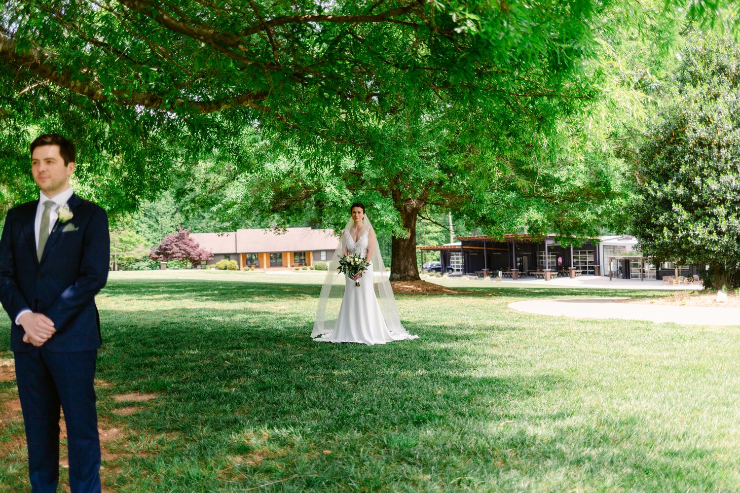 Wedding party members in formal attire gather on a lush green lawn during an outdoor summer celebration.