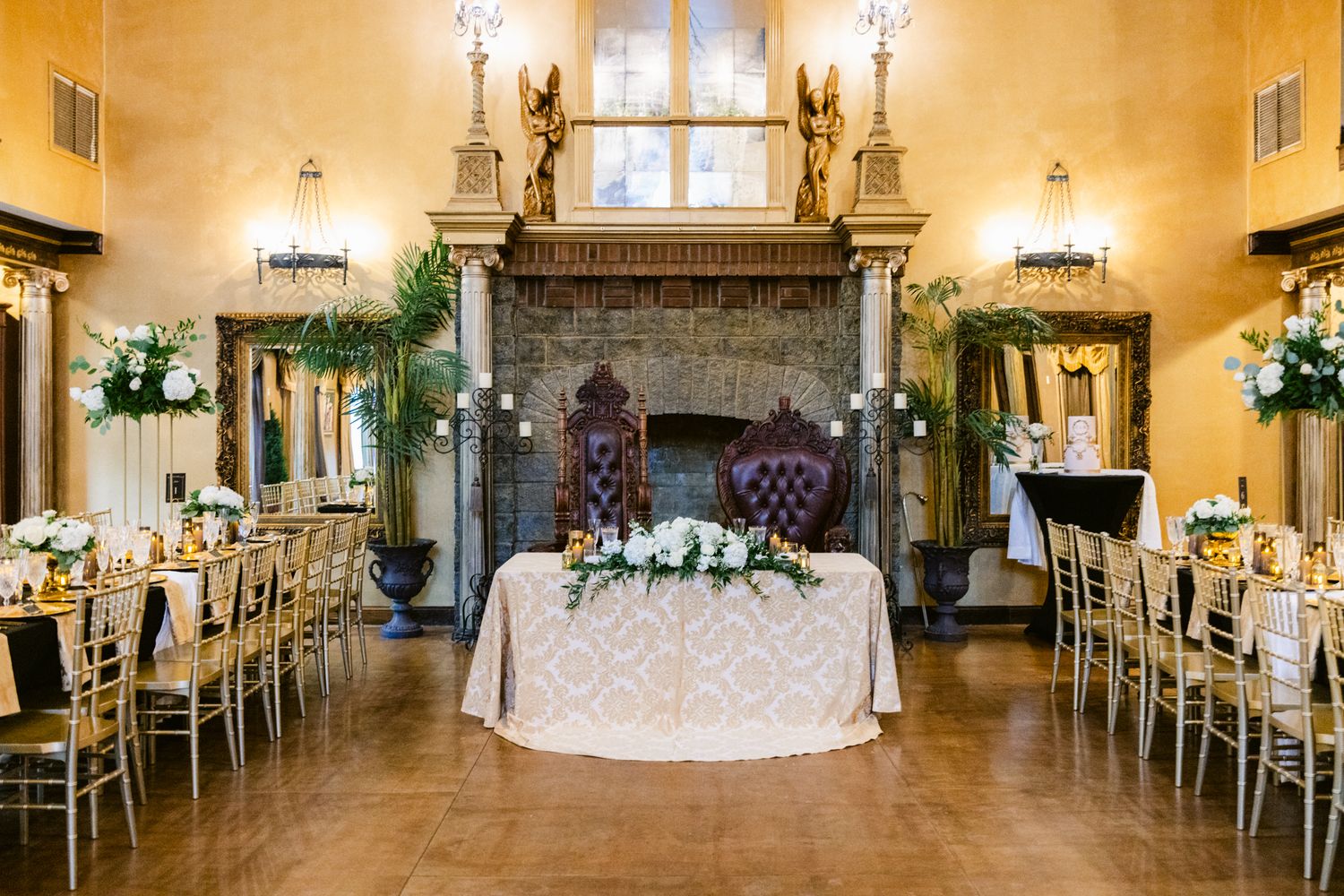 Panoramic view of an elegant wedding reception hall with white decor, chandeliers and floral arrangements.