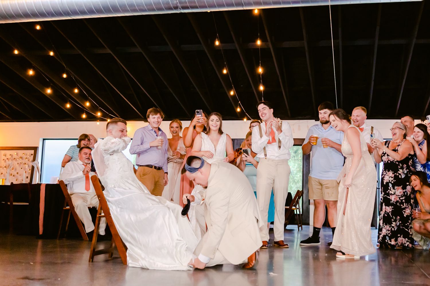 Wedding guests dance on a dark reception floor illuminated by warm overhead string lights.