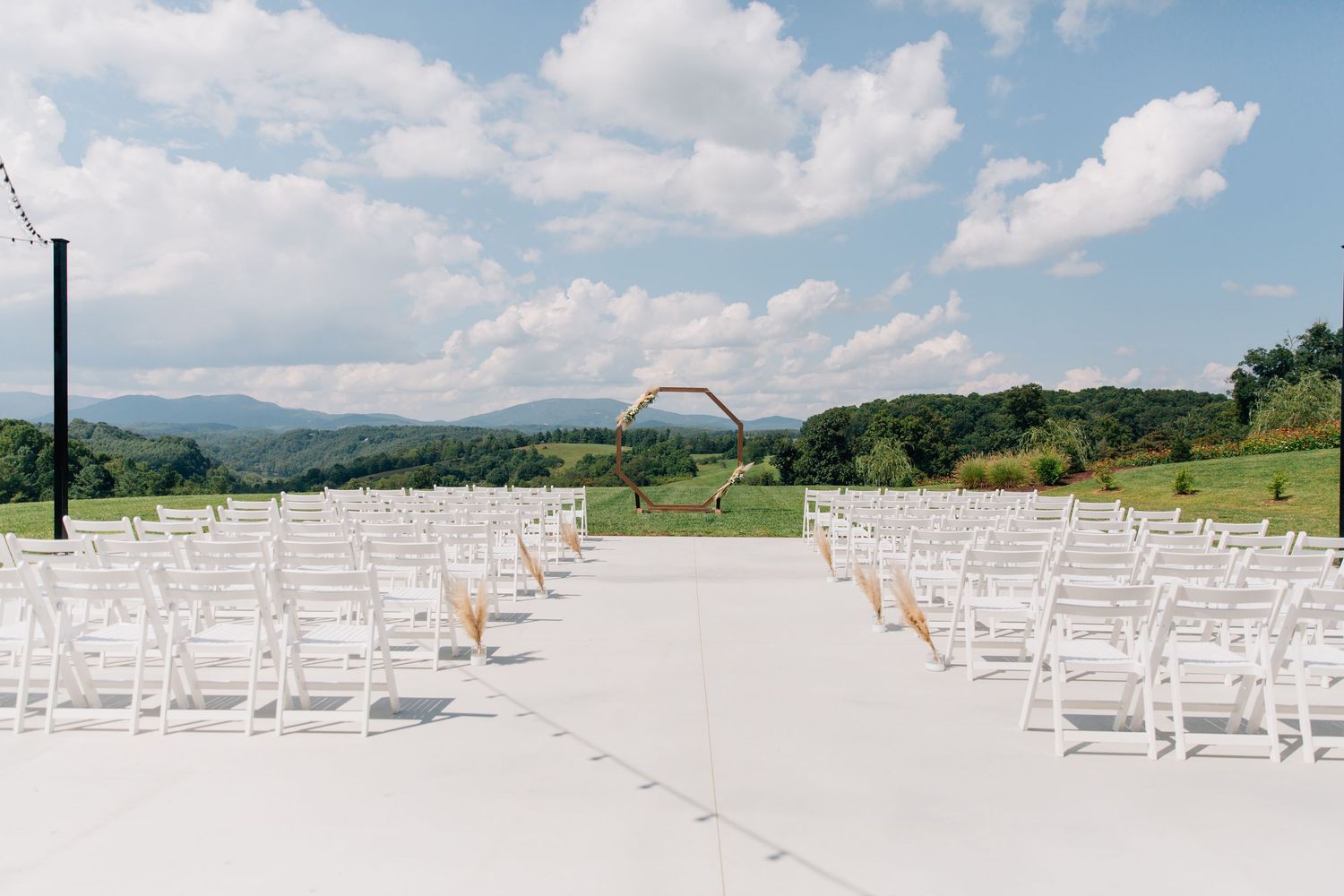 White wooden chairs arranged in rows for an outdoor wedding ceremony with mountains and cloudy sky in the background.