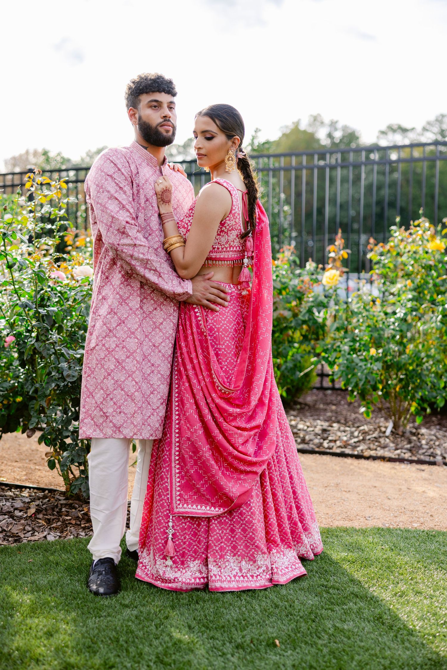 Couple in coordinated pink traditional Indian attire embracing in a blooming garden.
