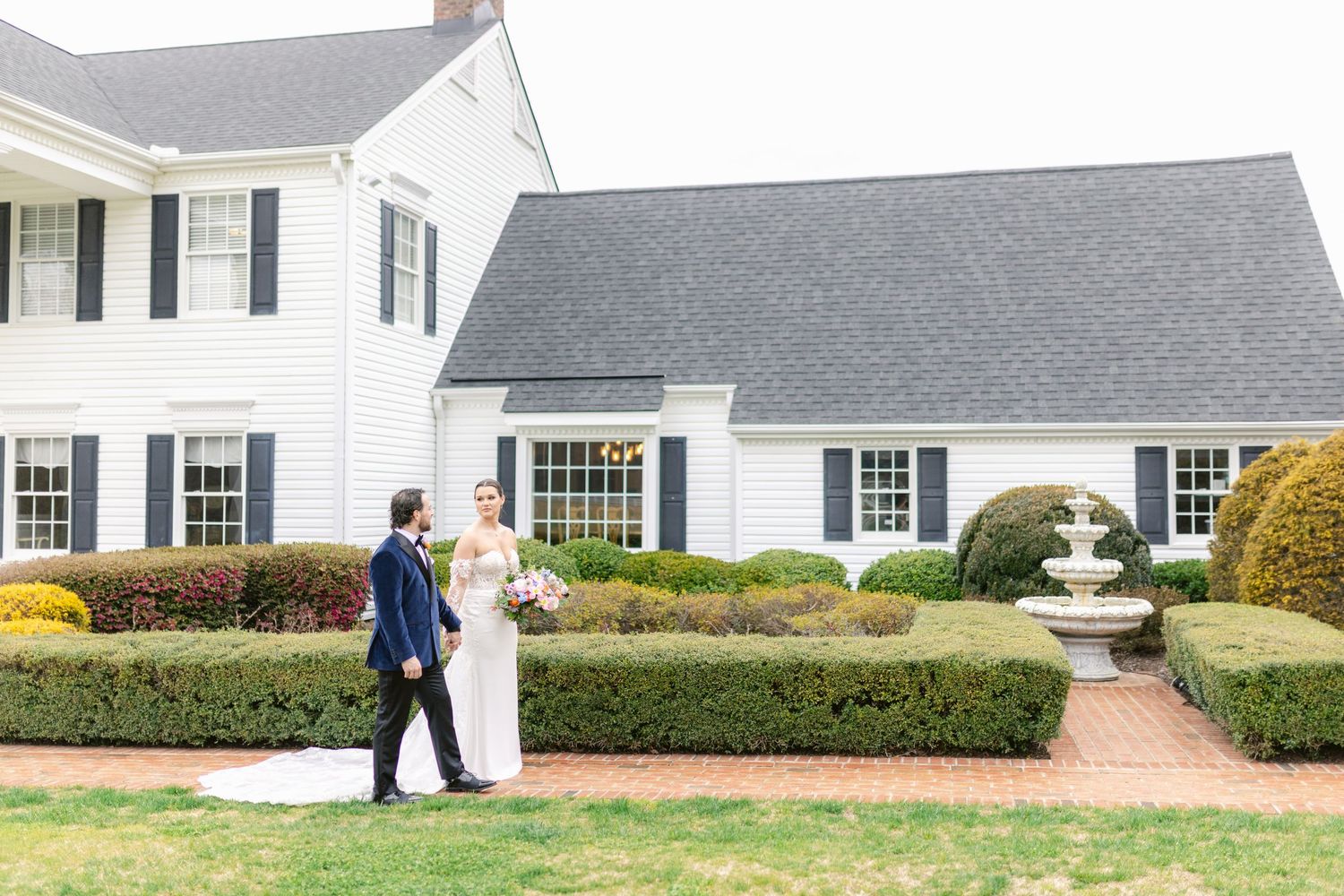 Professional landscaper using a leaf blower to clean up yard debris around a white residential home with black shutters.