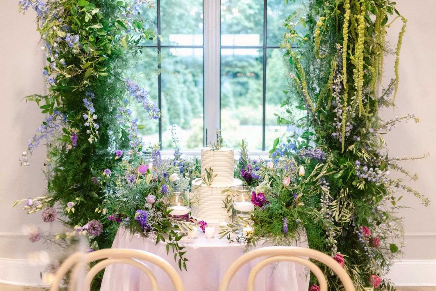 Elegant wedding reception table setting with climbing vines and floral arrangements framing a window in natural light.