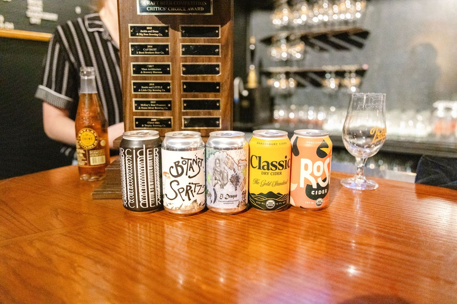 Various craft beer cans and glasses displayed on a wooden bar counter at a brewery or taproom.