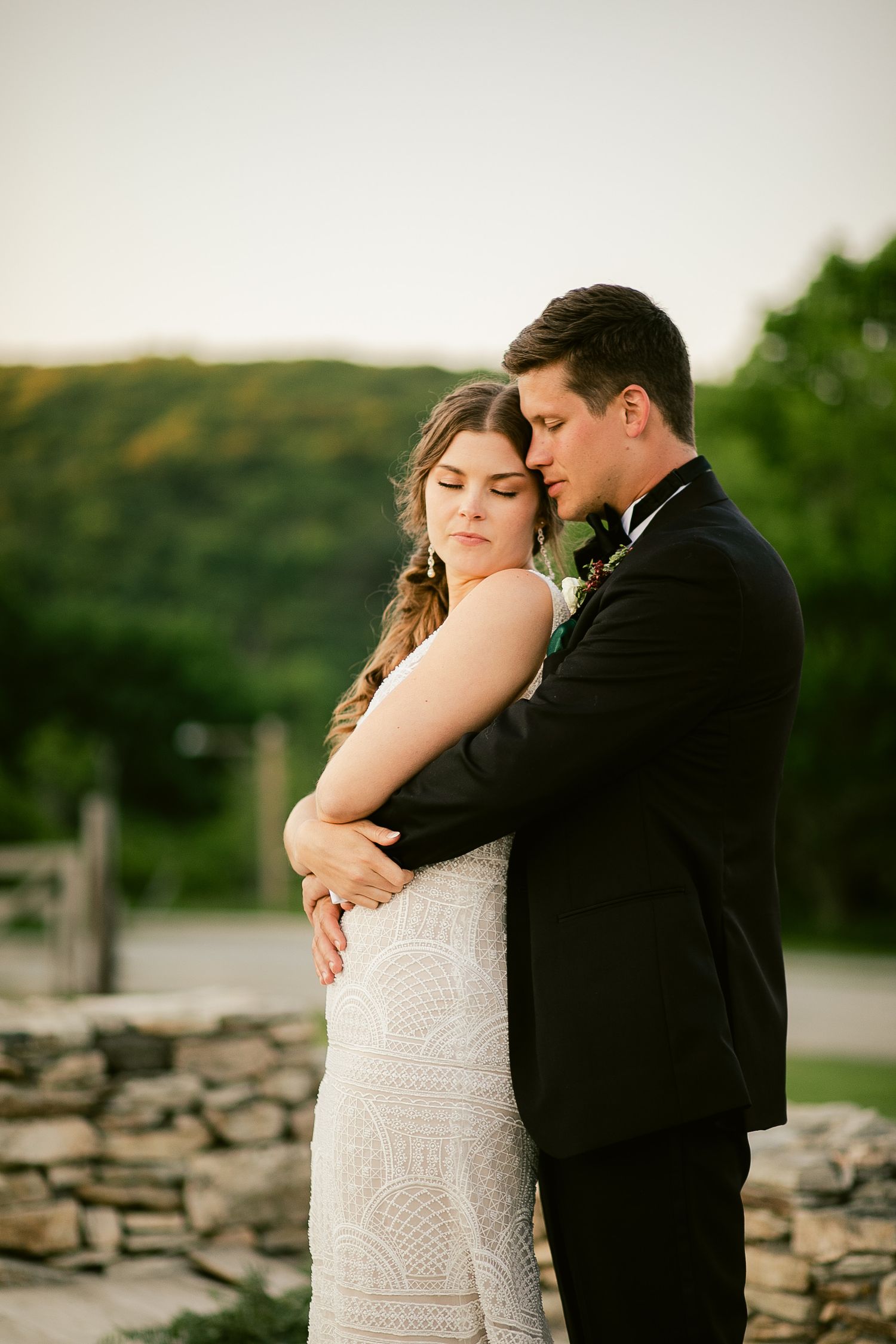 Newlyweds share an intimate moment near a stone wall during golden hour at their outdoor wedding.