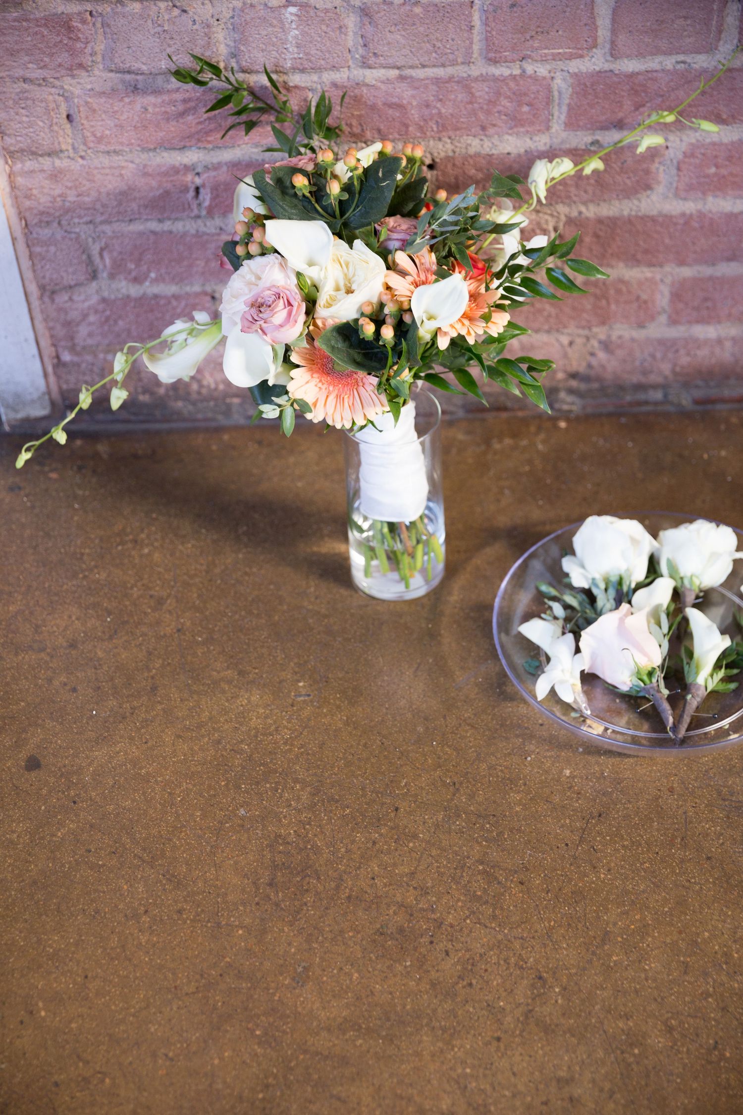 Small floral arrangements in glass jars sit against a rustic brick wall on a brown textured surface.