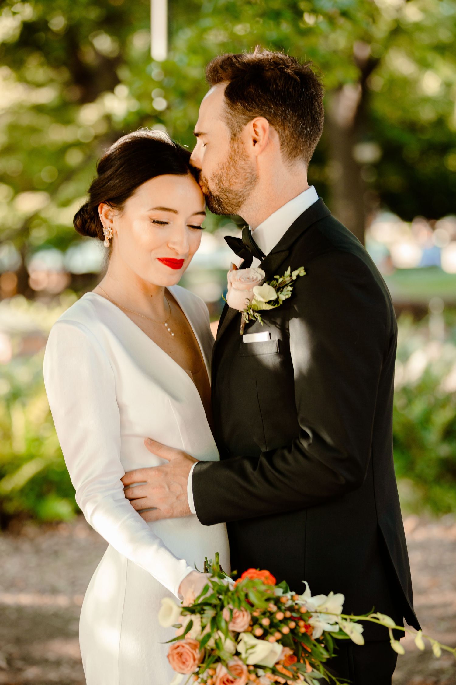 A romantic wedding moment captured outdoors with a classic white dress and black tuxedo against a natural garden backdrop.