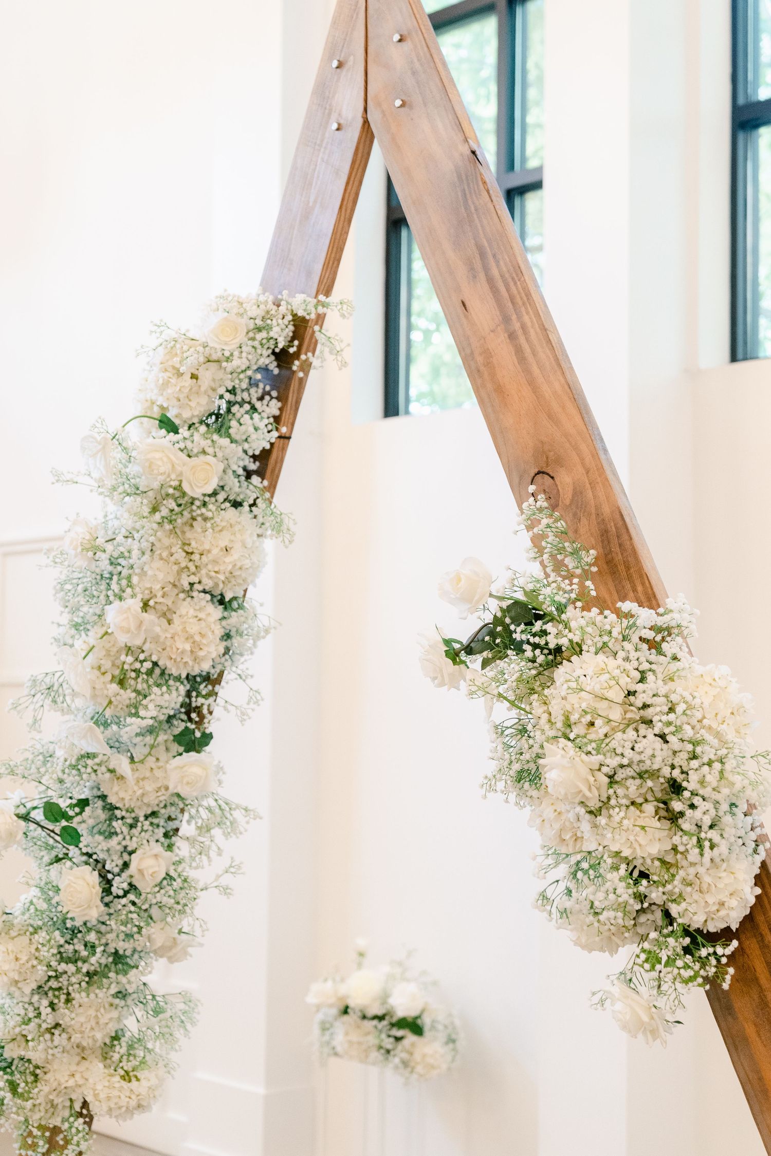 White floral arch decoration with delicate baby's breath and roses against white wall.
