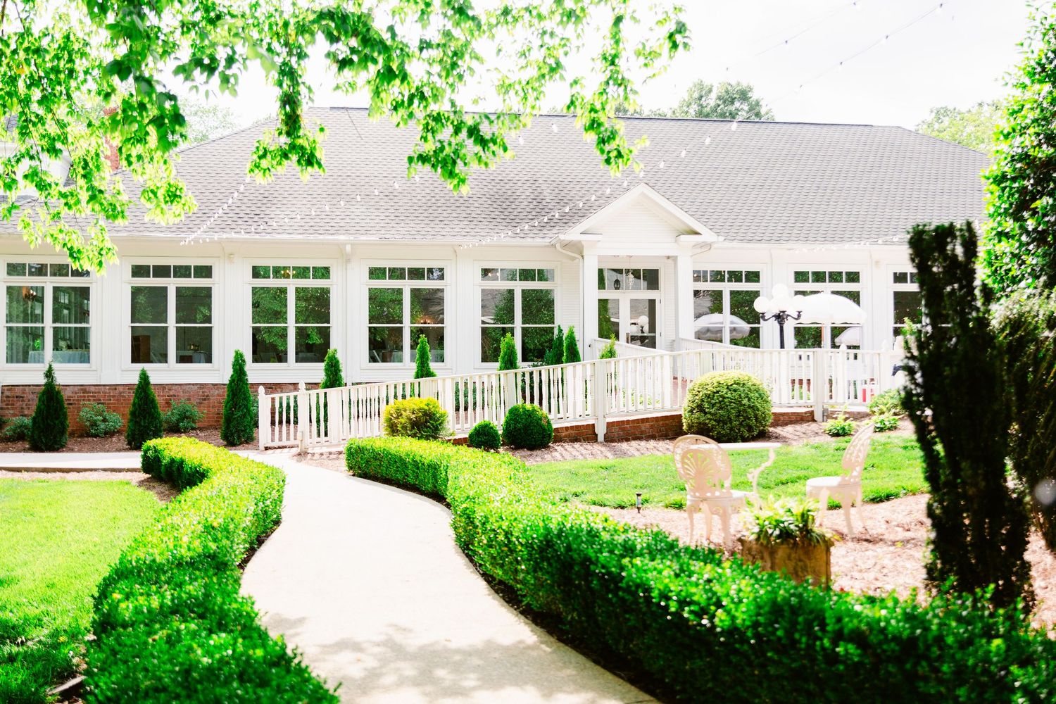 White event venue building with large windows and landscaped gardens in a lush green setting.