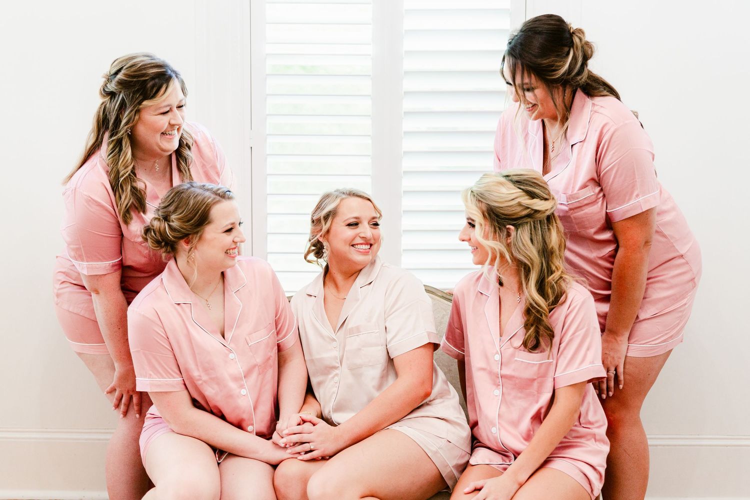A group in matching pink robes share joyful moments while getting ready together in a bright white room.
