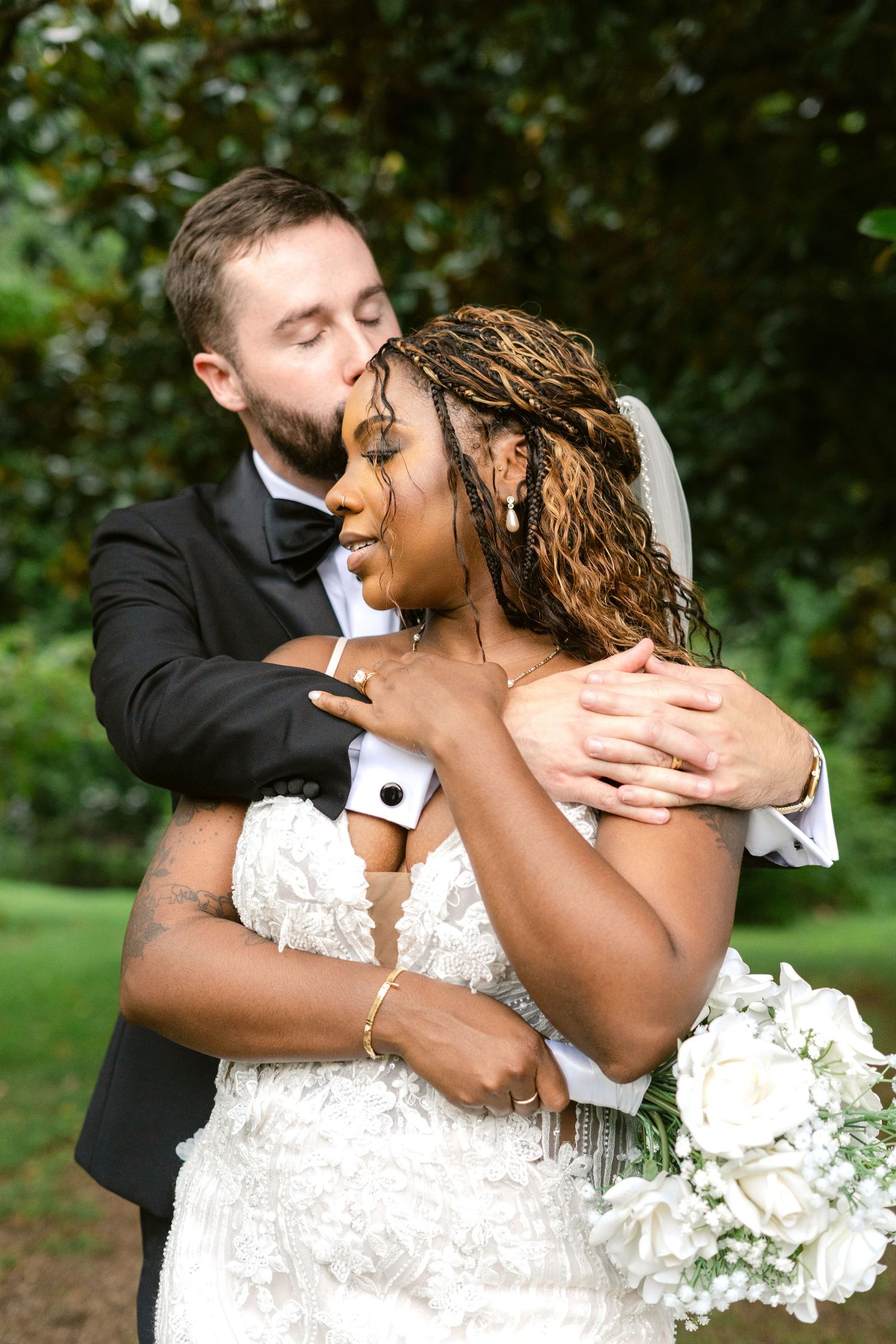 A romantic wedding moment captured in a lush garden setting showing a tender embrace between newlyweds.