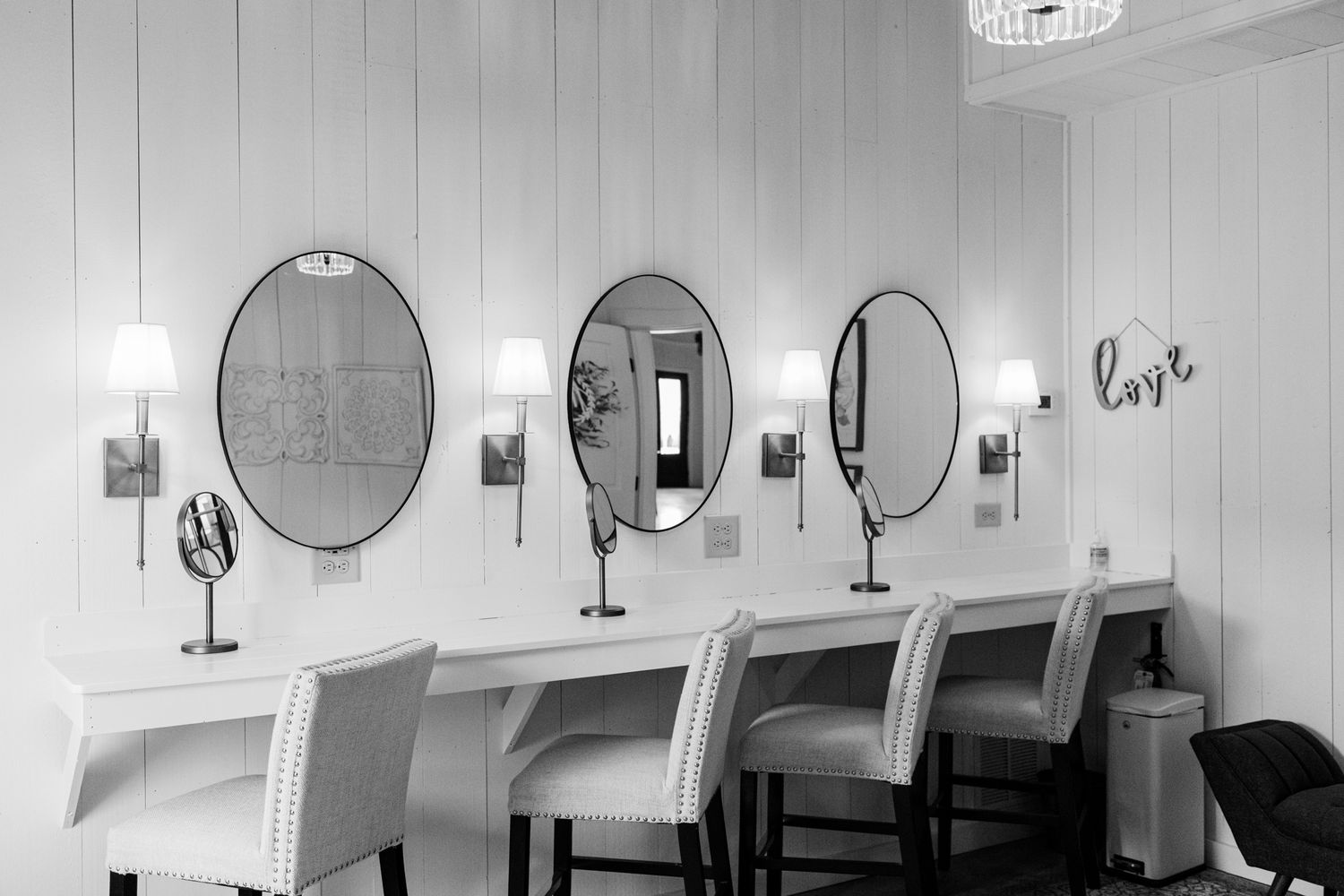 Black and white photograph of a vintage beauty salon interior with chairs, mirrors, and hair dryers lined up against the wall.