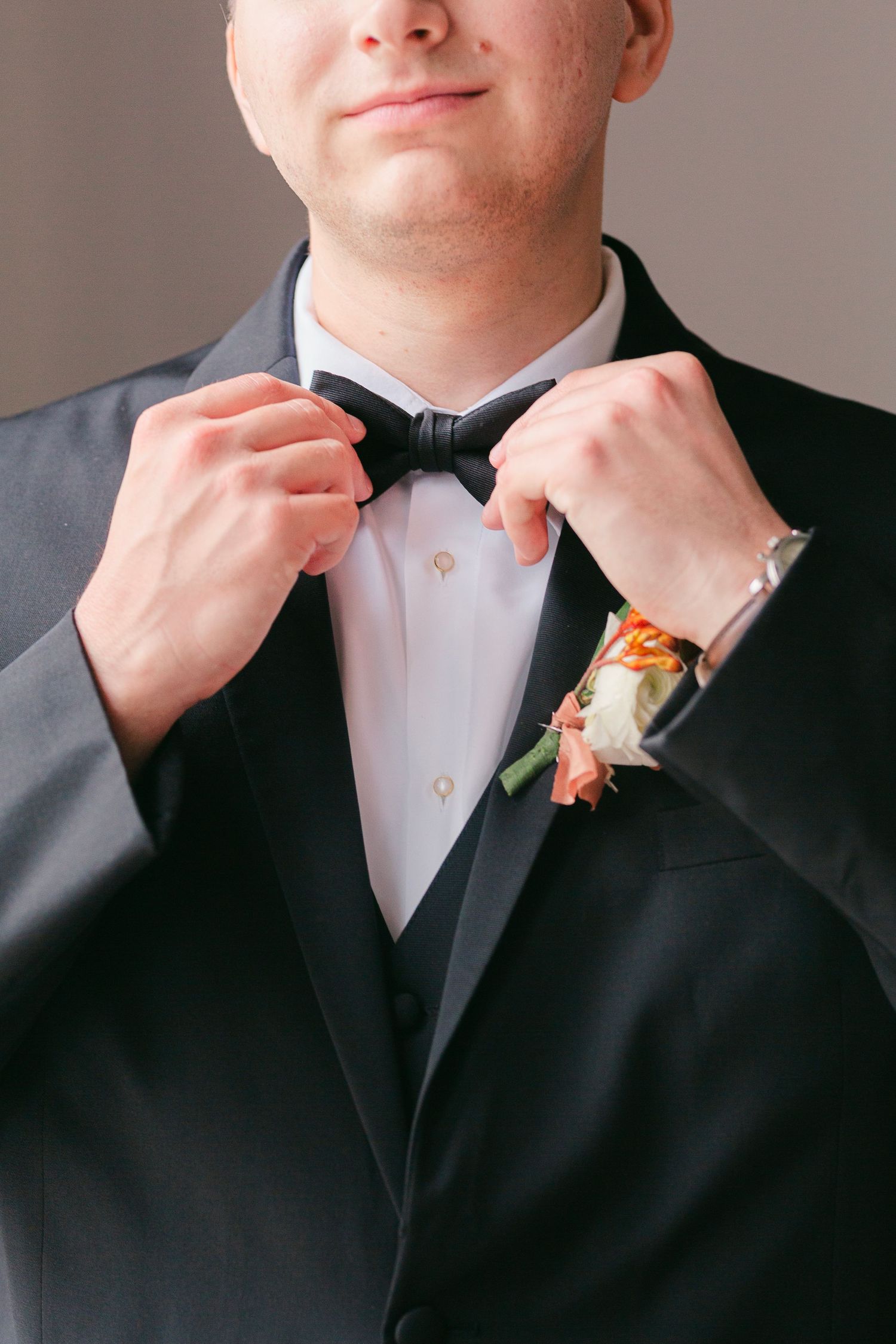 Close-up series of someone adjusting a black bow tie while wearing a formal tuxedo with a boutonniere.