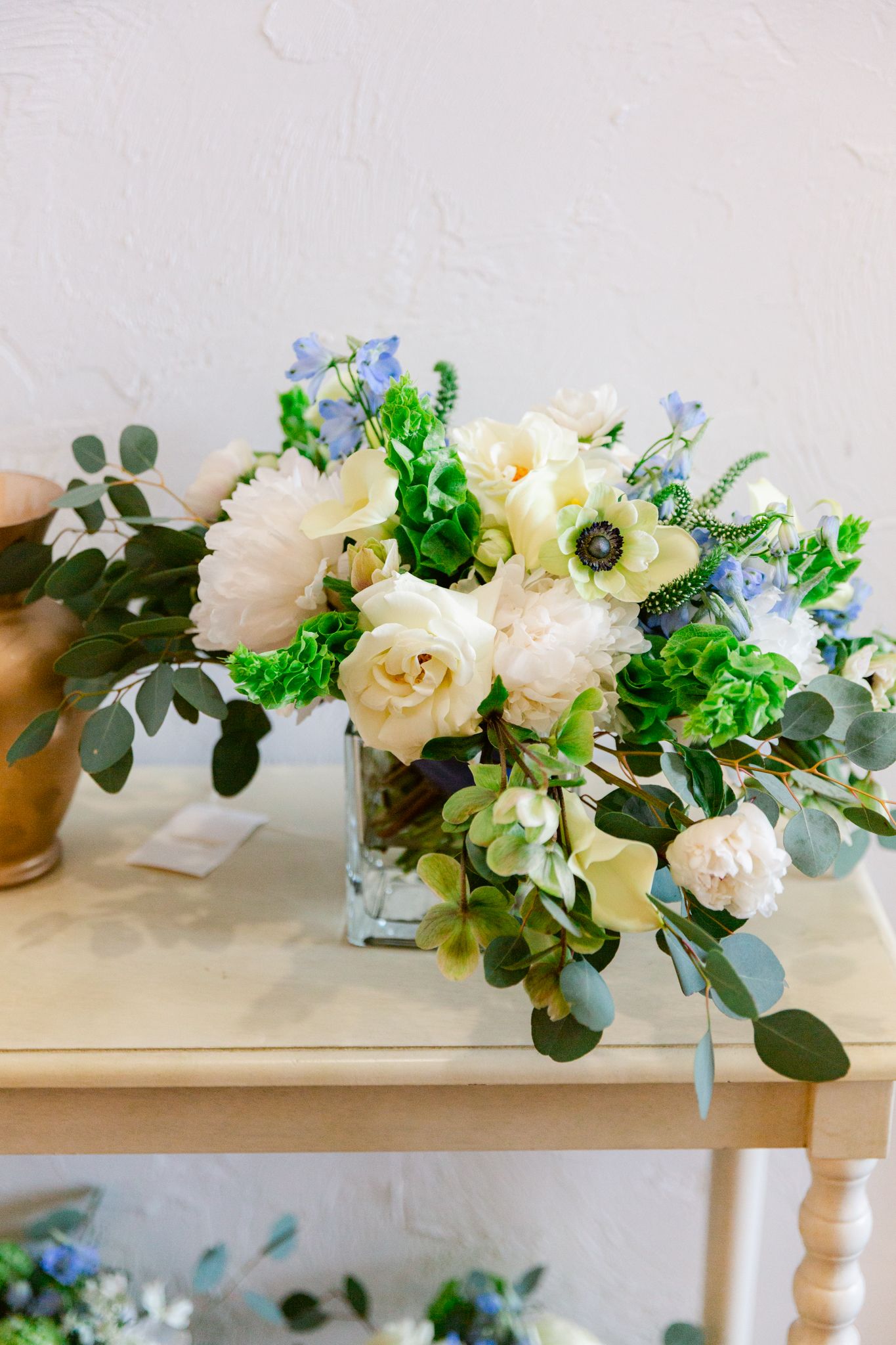 Elegant floral centerpiece with white roses, blue forget-me-nots, and eucalyptus leaves arranged in a low profile design.