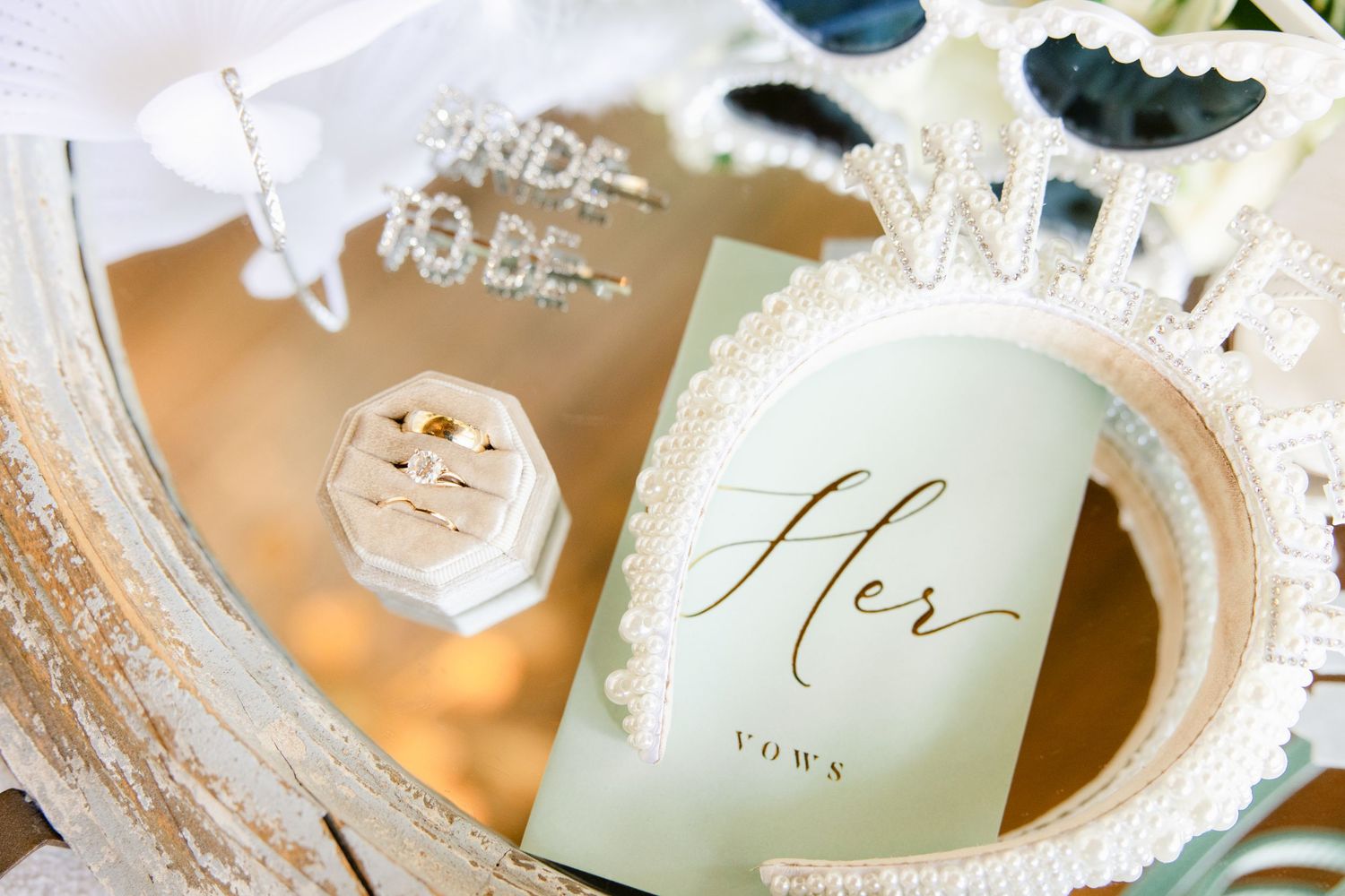 Close-up details of wedding invitations and paper goods in soft sage green and white with metallic gold lettering.