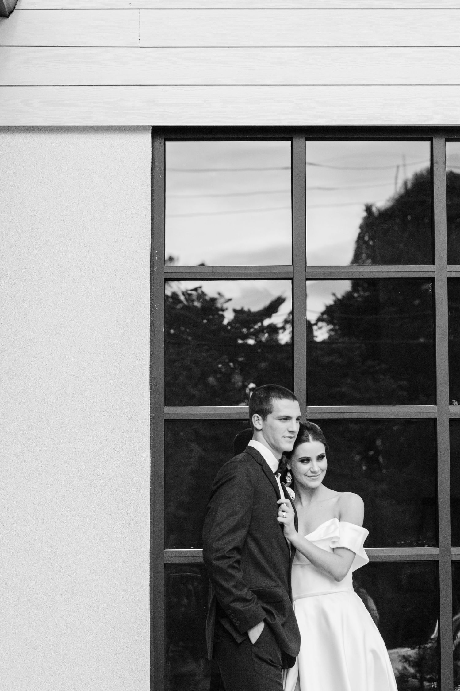 A black and white wedding photo showing a couple standing together in front of a large geometric window.